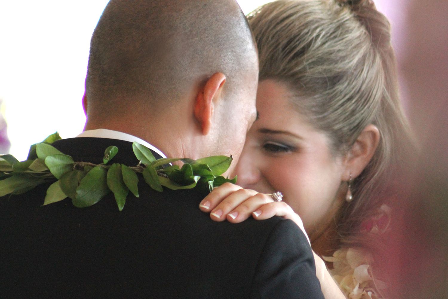Close-up of intimate wedding embrace with greenery detail on groom's shoulder.