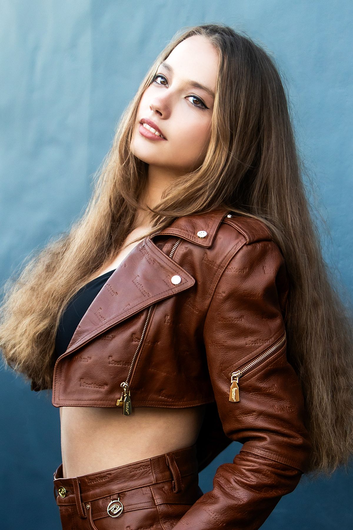 Fashion portrait with brown leather cropped jacket against blue background.