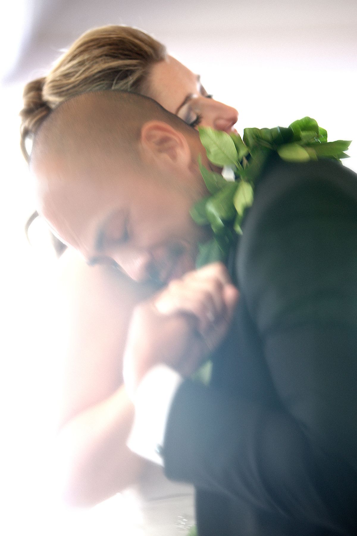 Bride and groom embrace in an intimate soft-focus portrait with delicate greenery.