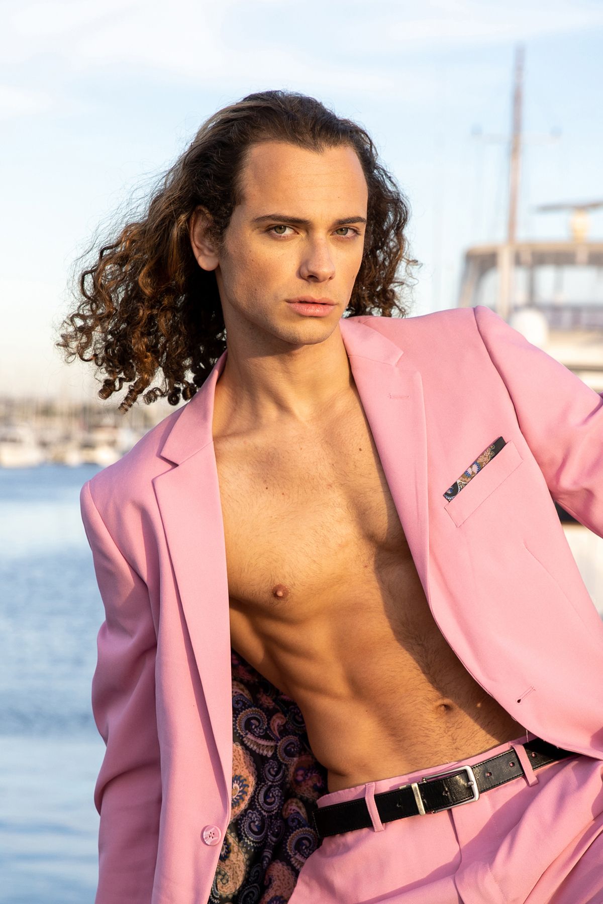 Model in pink blazer poses against waterfront backdrop.