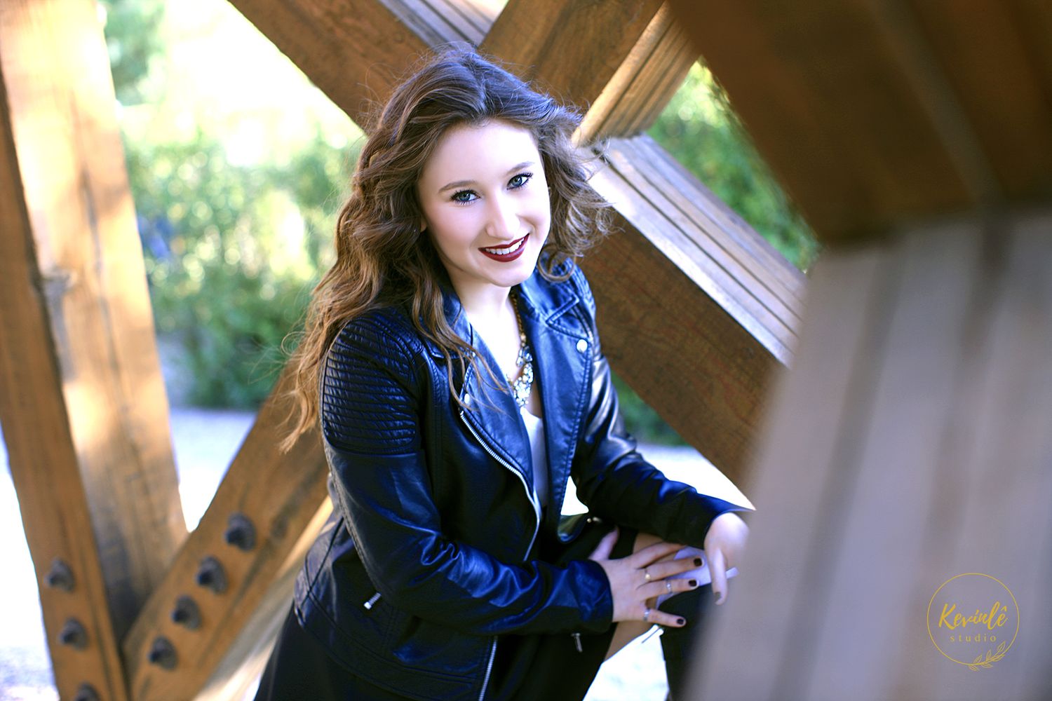 Senior portraits with person in dark jacket posing against wooden structure.