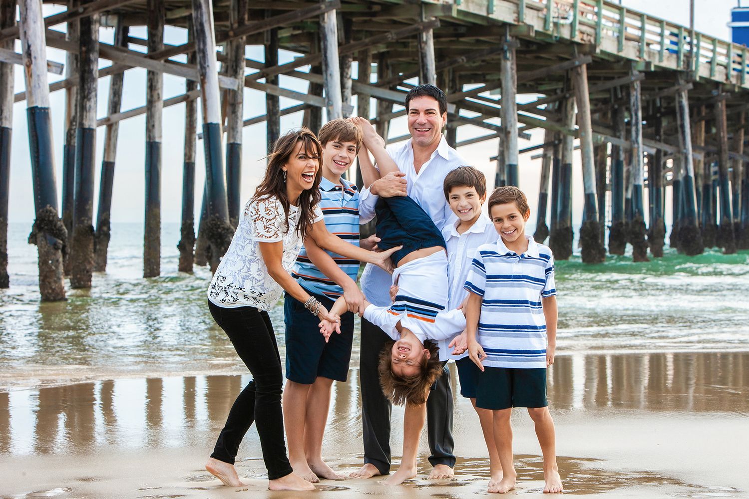 Group enjoying a playful moment together on the beach by a wooden pier in casual summer attire.