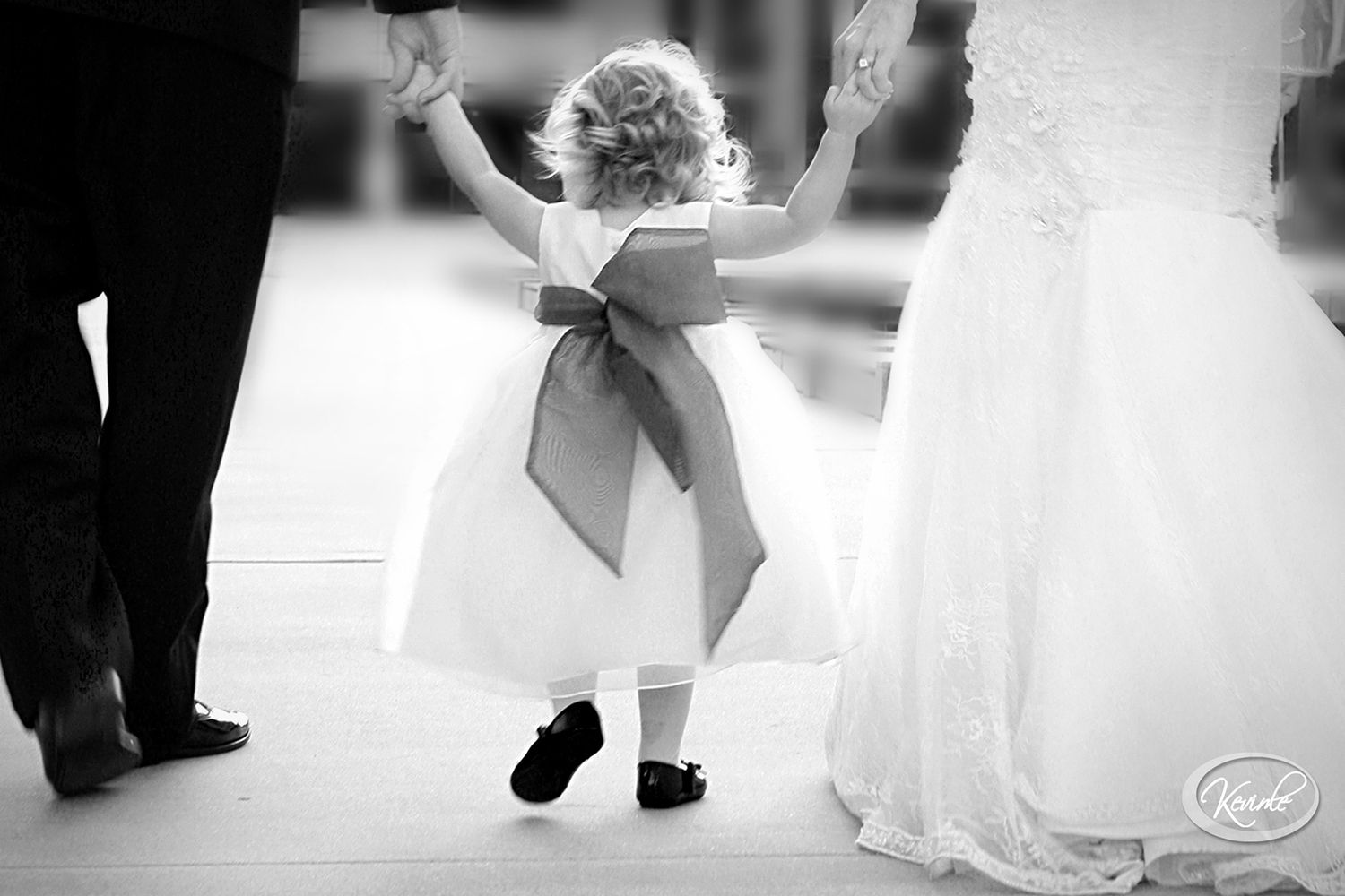 A small child in a white dress with a bow dances at a wedding reception.