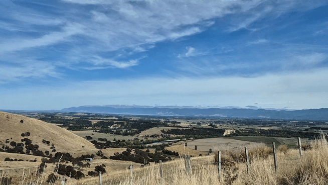 Rolling golden hills overlook a scenic valley landscape with mountains in the distance under a blue sky at Whitimanuka by August and Vine