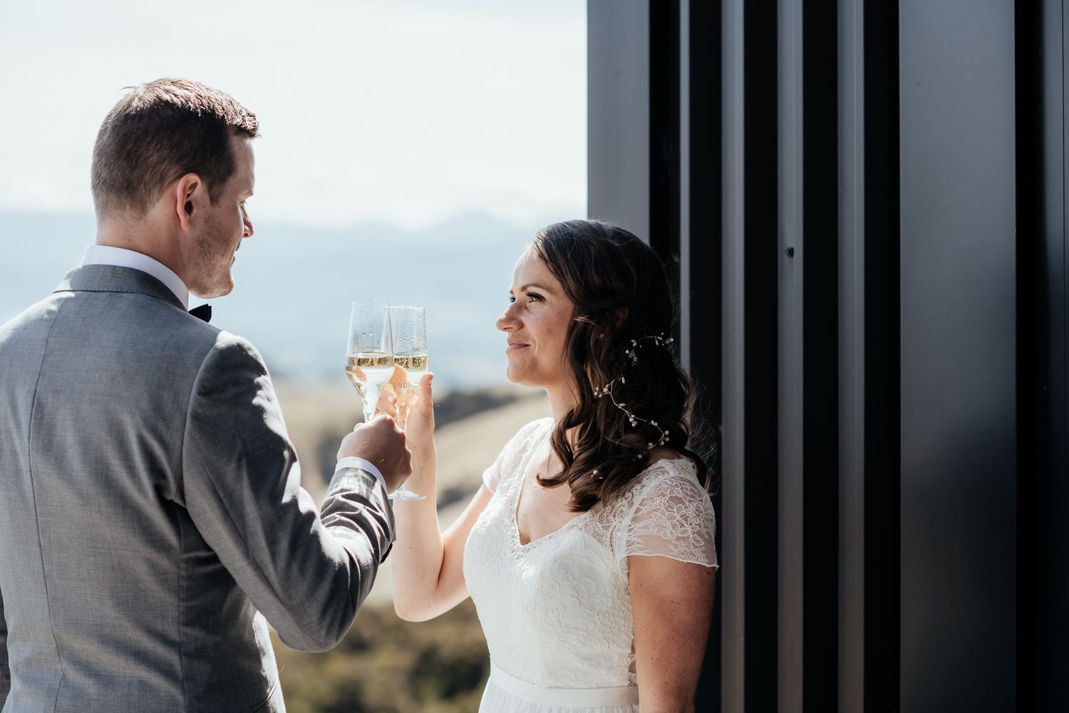 A couple toasts with champagne glasses at Whitimanuka overlooking valley views during a wedding celebration by August and Vine