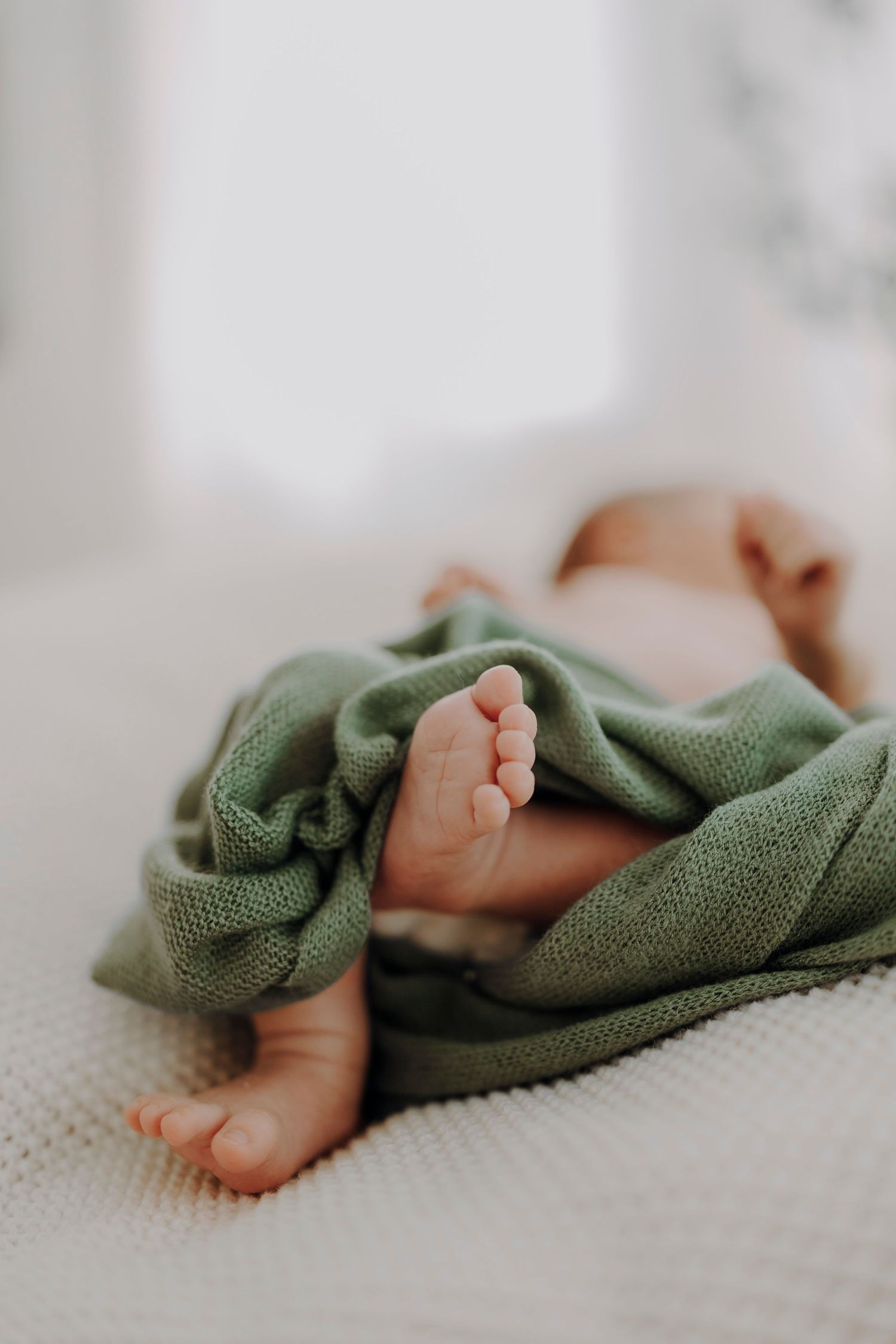 Tiny baby feet peek out from under a soft green blanket.