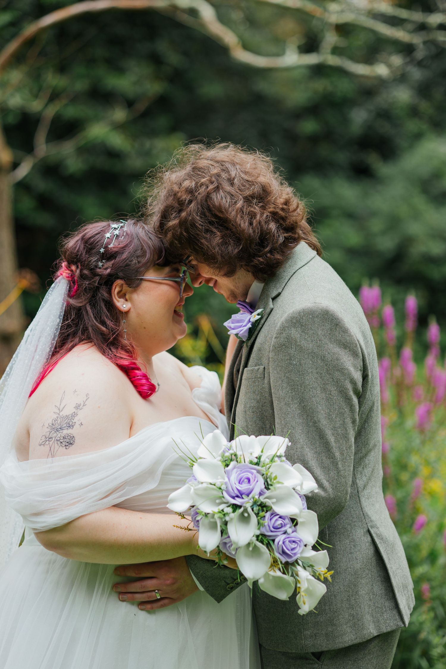 Intimate wedding portrait in a garden with purple wildflowers blooming in the background.