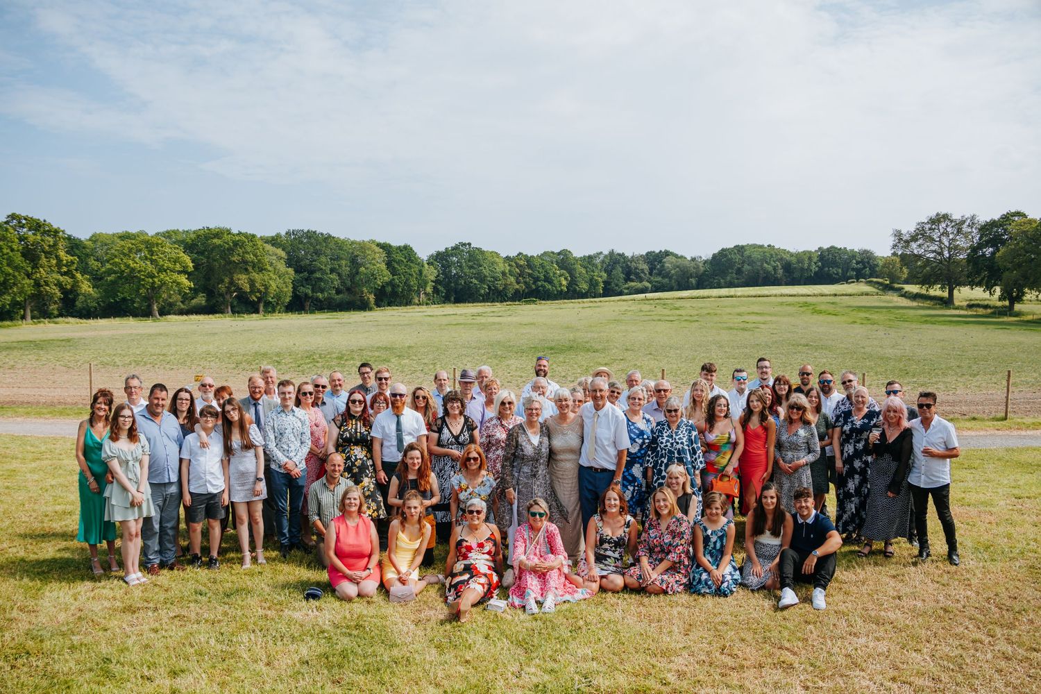 Large wedding party group photo taken on a sunny day in a sprawling green field.