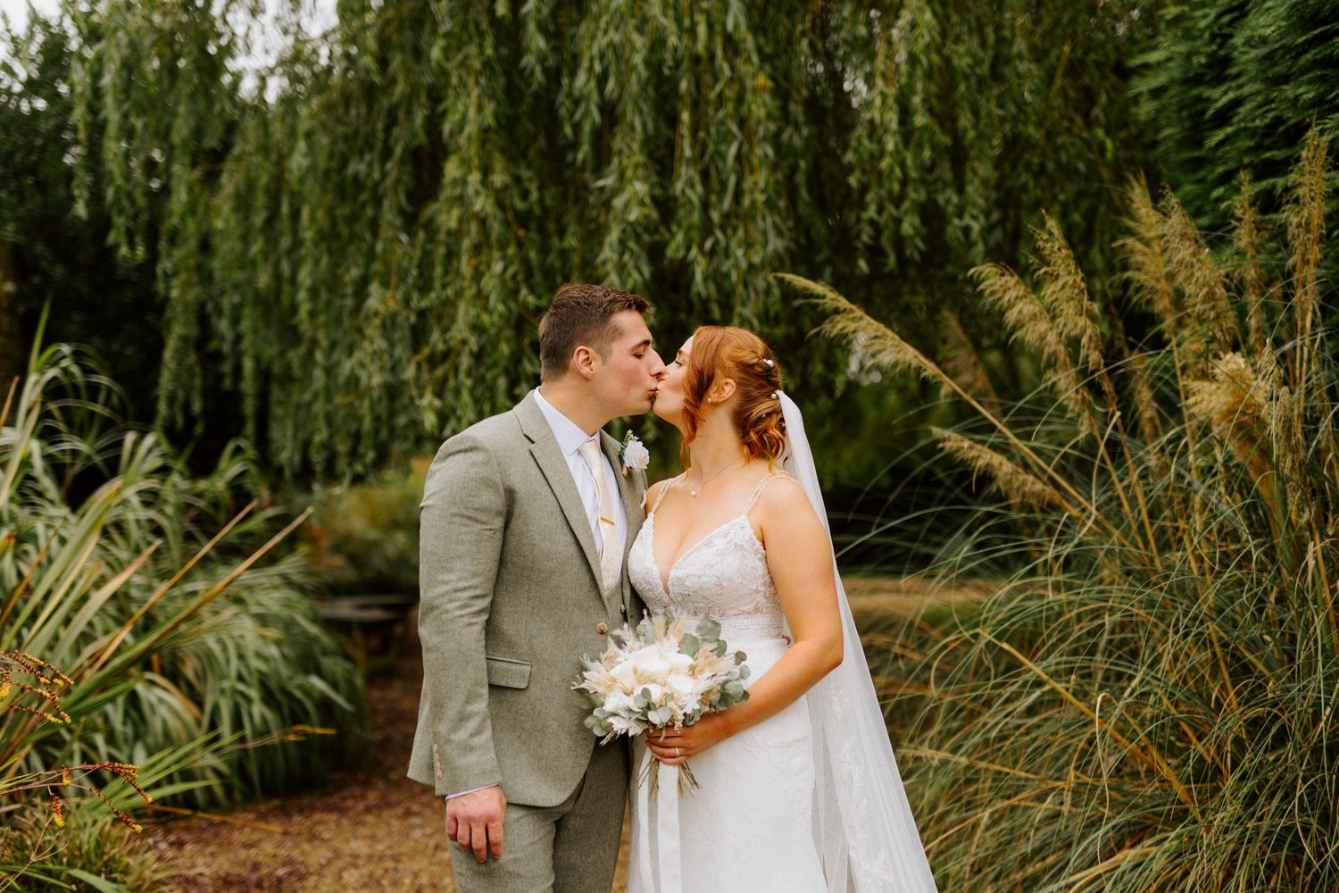 Newlyweds share a tender moment among tall grasses and weeping willows.