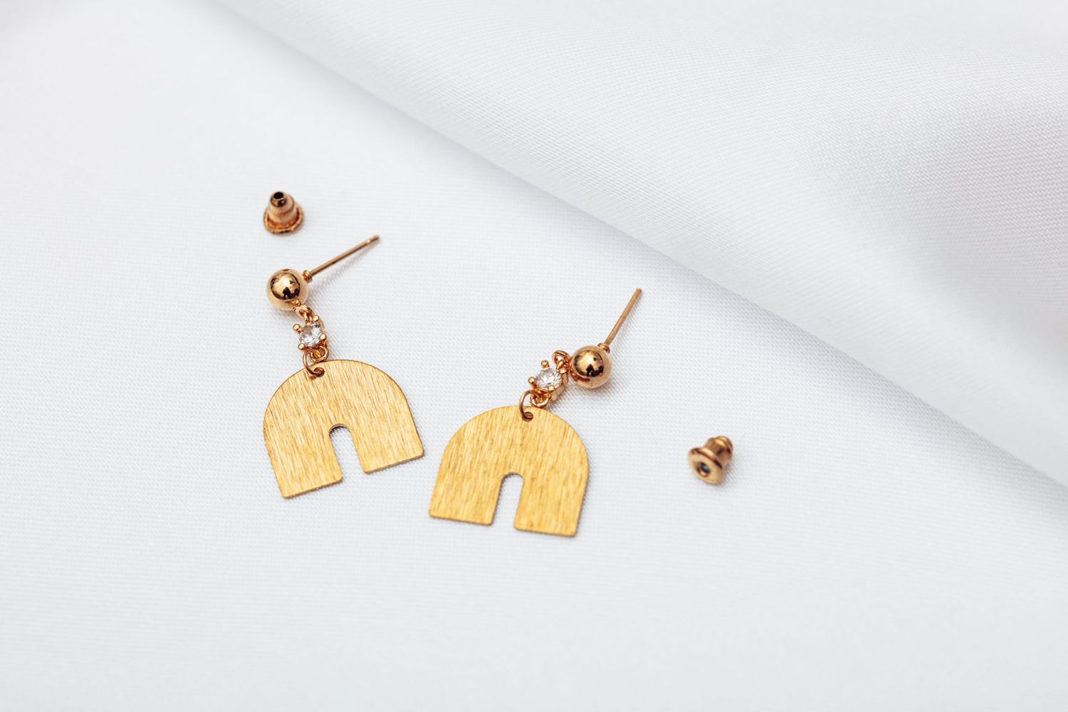 Gold elephant shaped earrings with stud posts rest on a white textured surface.