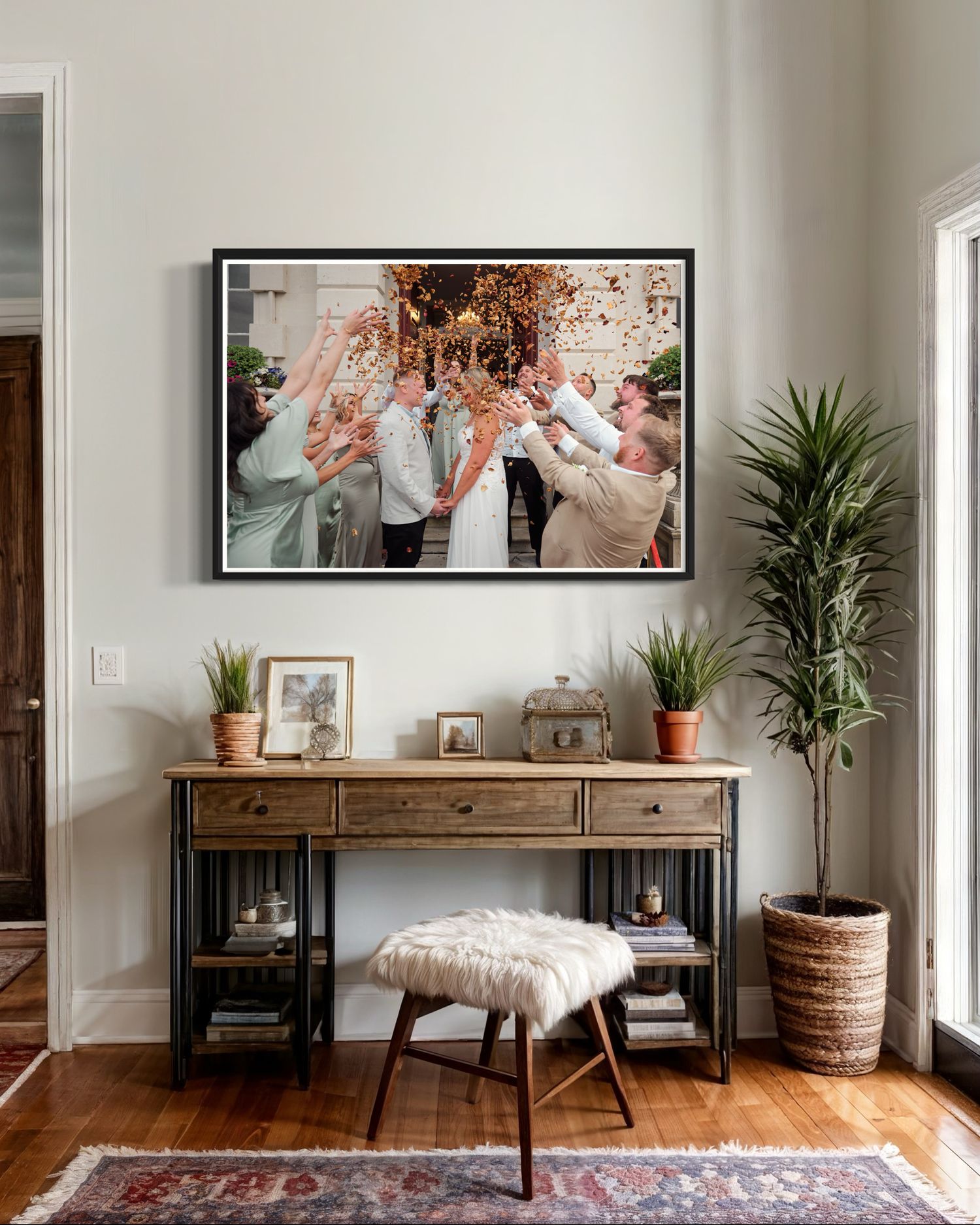 Modern home interior with rustic console table, large framed photo, plants and fur stool against neutral wall decor.