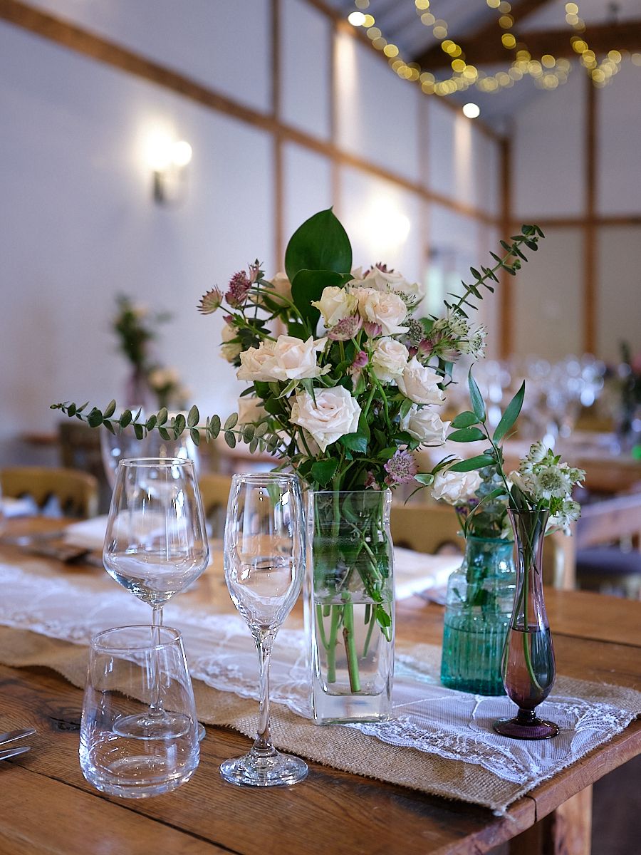 Elegant wedding table setting with glass vases featuring white flowers and eucalyptus on lace table runners.