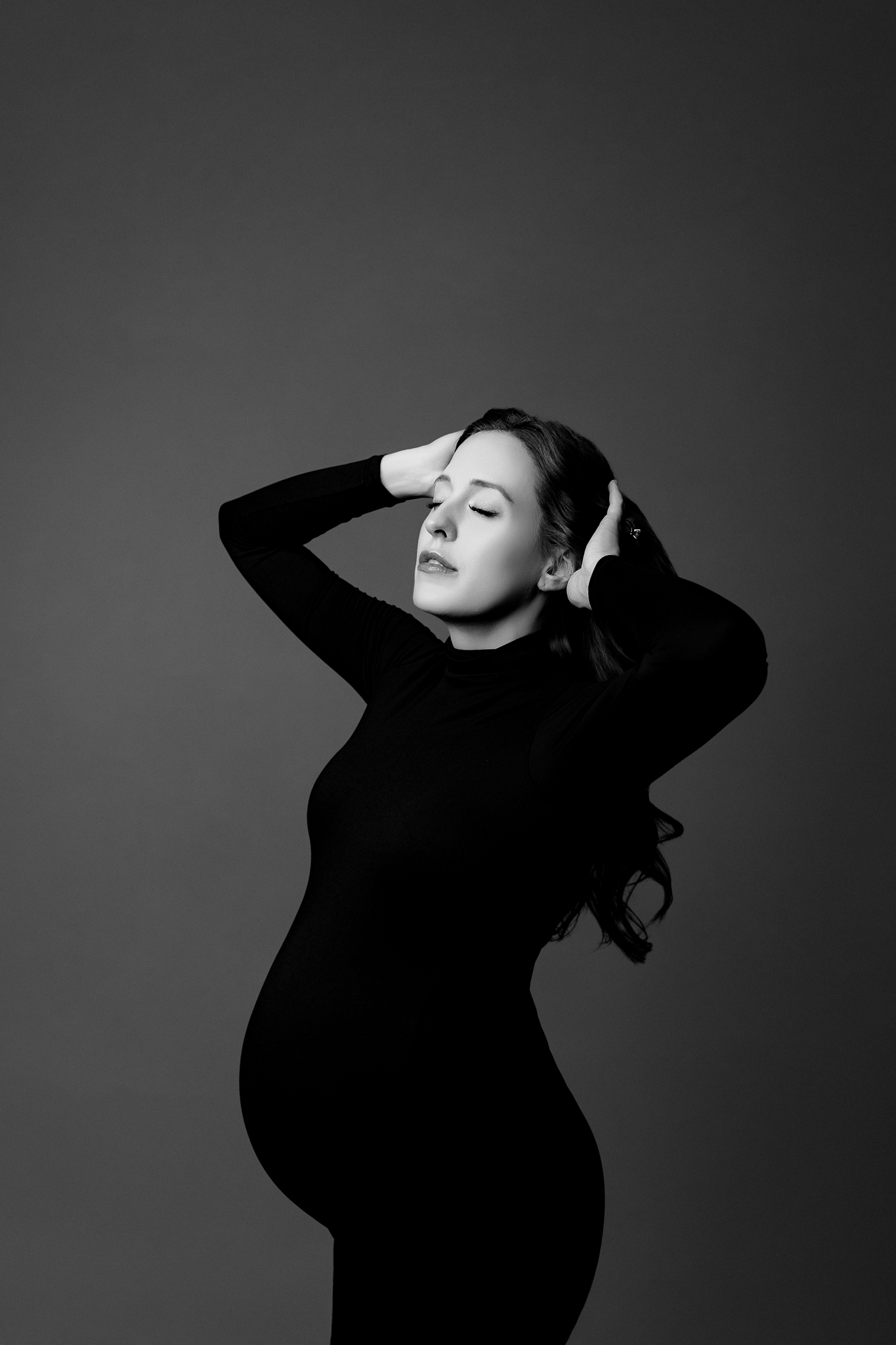 Black and white fine art maternity portrait of a pregnant woman wearing a form-fitting black turtleneck dress.