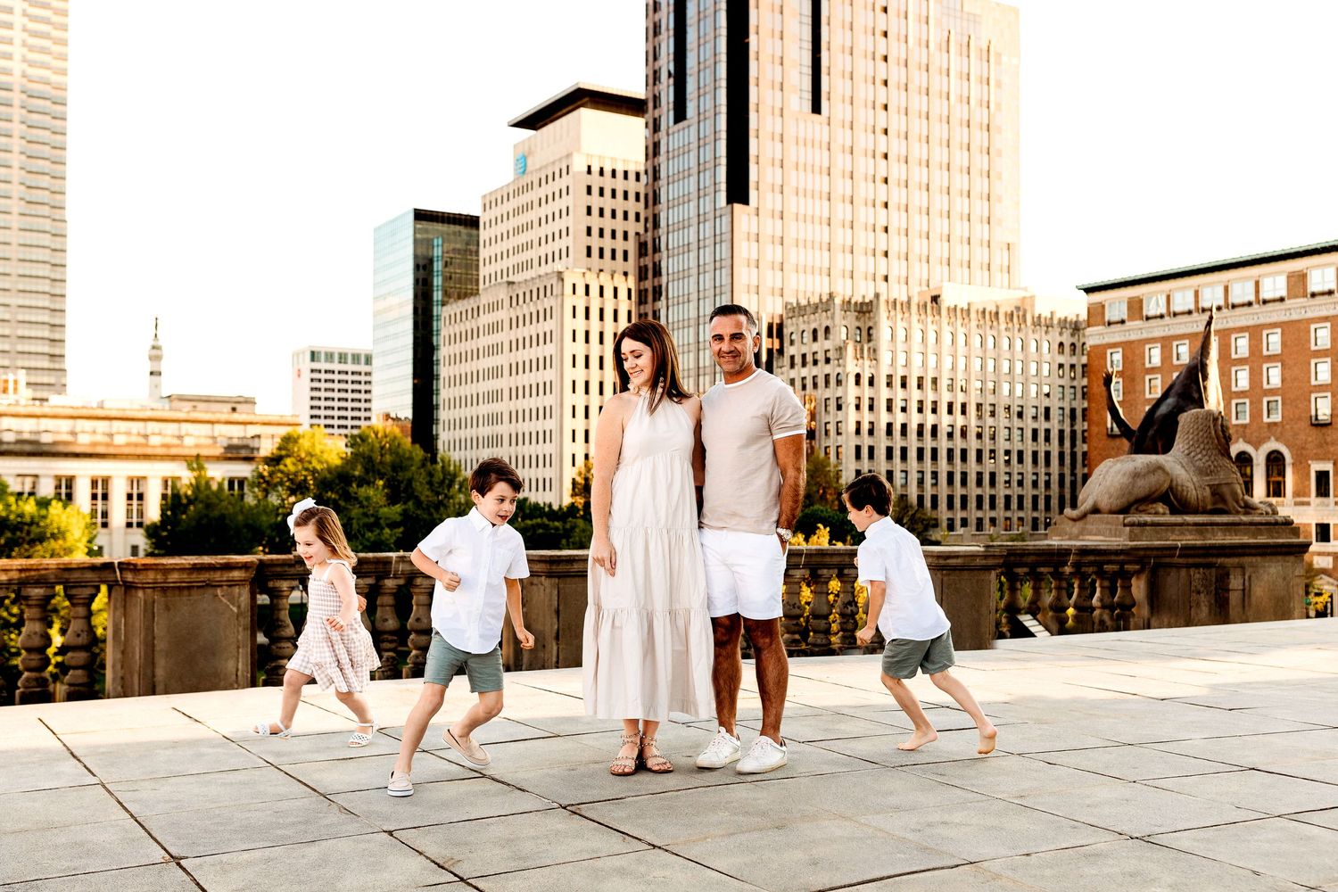 A smiling couple stands together on a city rooftop, surrounded by four playful children. Downtown Indianapolis Indiana is in the background