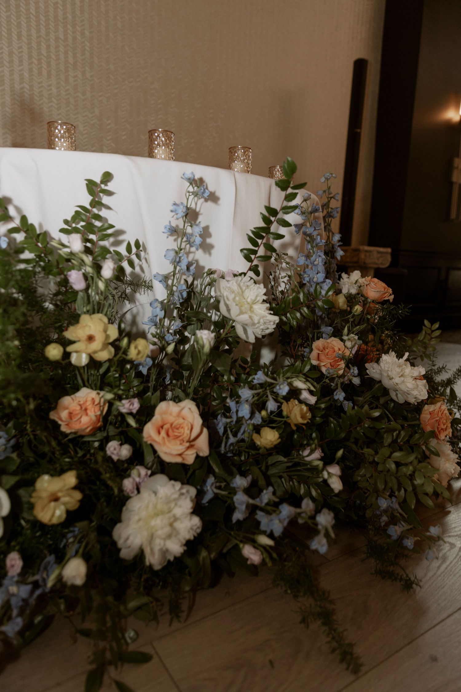 Elegant floral arrangement with peach roses, white carnations, and delicate blue delphinium against a white backdrop.