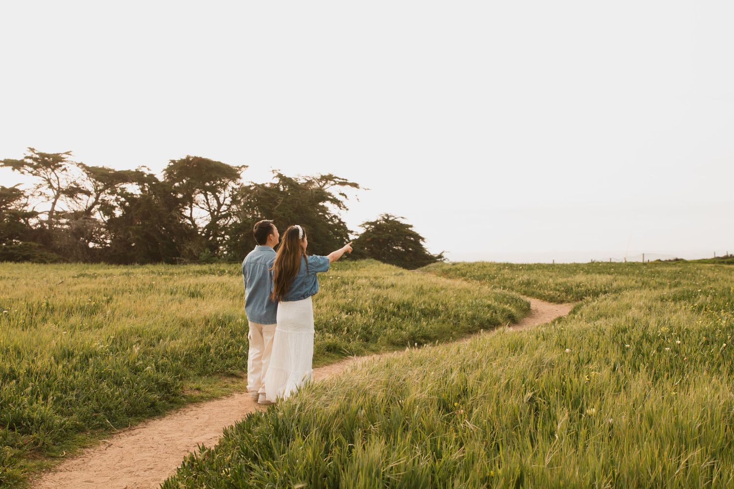 Two figures walking on a scenic hiking trail through golden grass fields under bright sky.