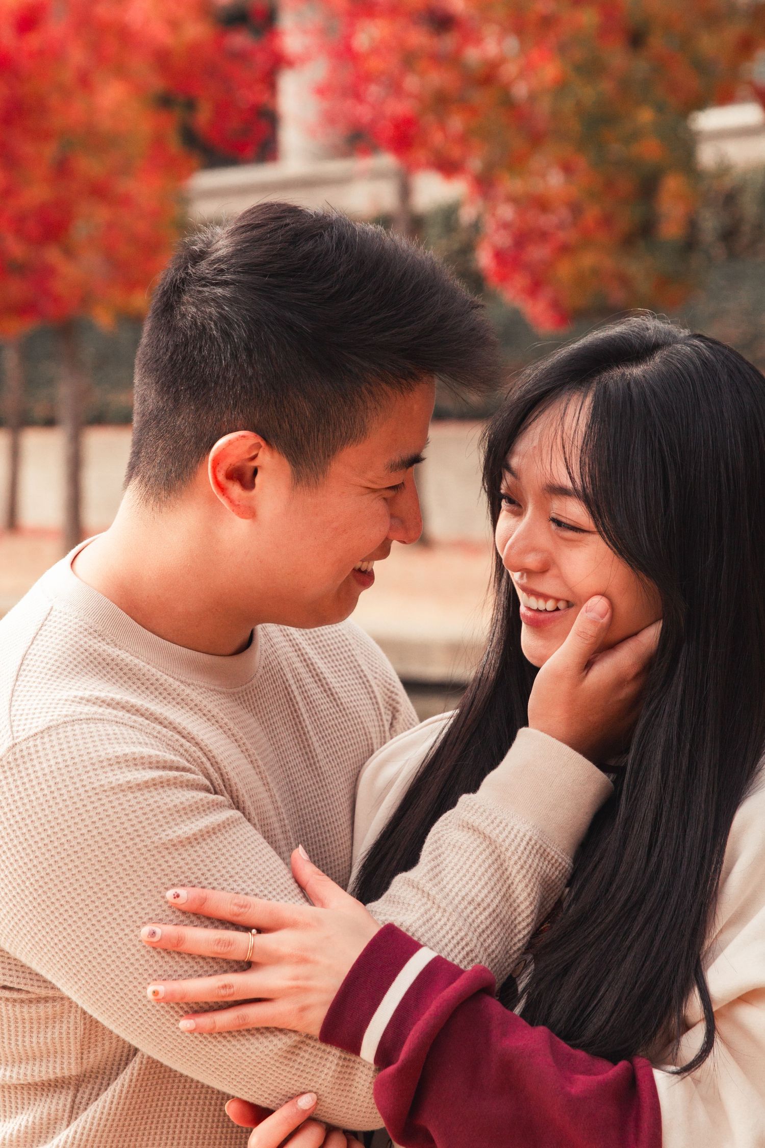 A romantic couple shares an intimate moment together against a backdrop of vibrant red autumn foliage.