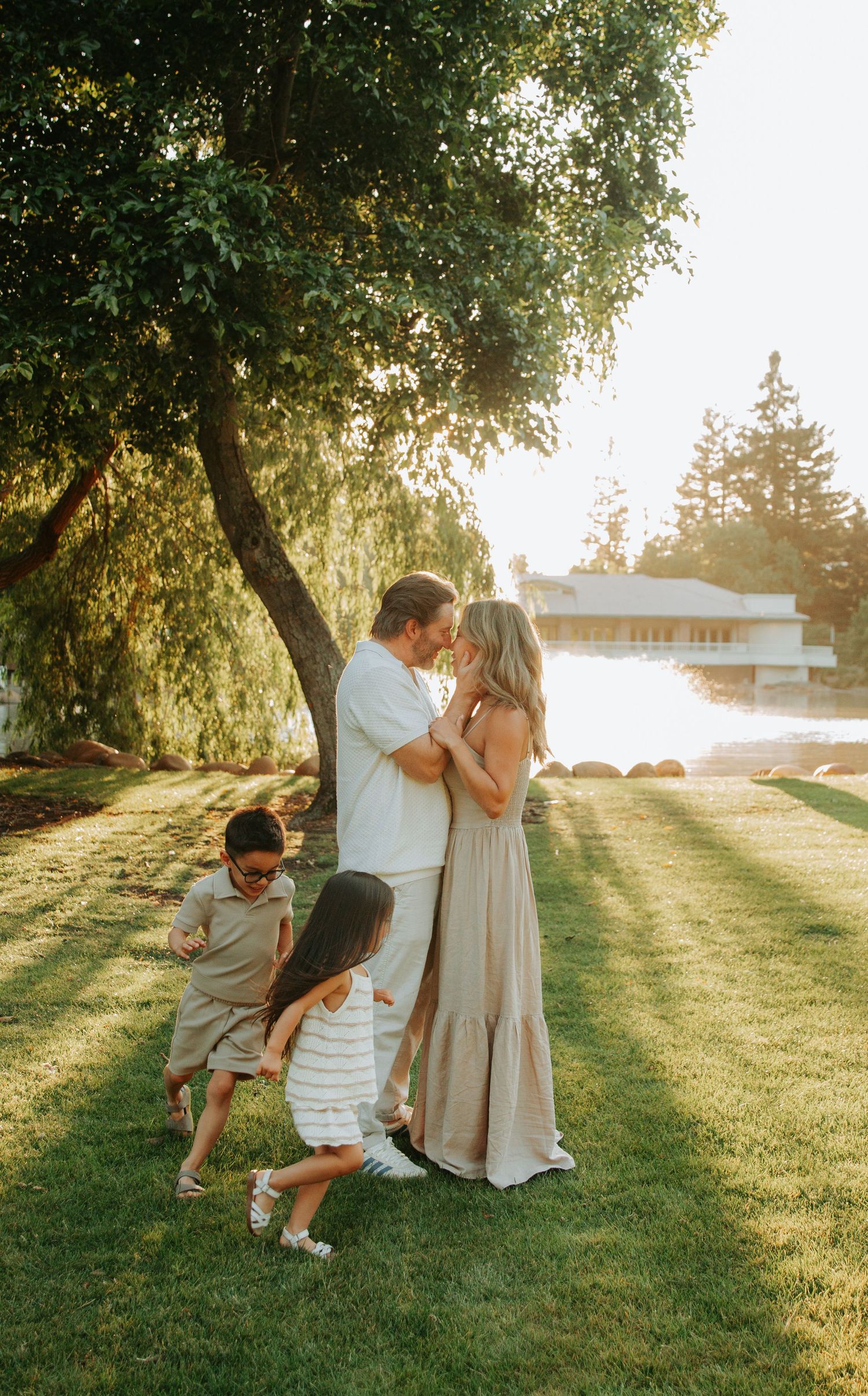 A loving family spends golden hour together in a sun-dappled backyard with willow trees and green grass.
