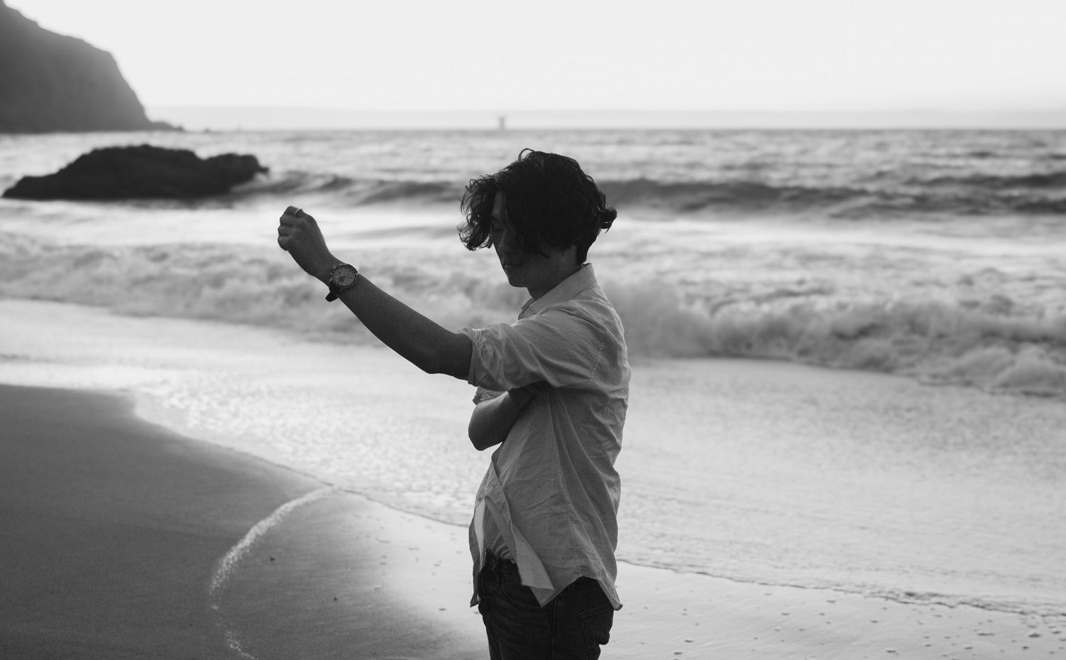 Black and white photo of someone dancing on a beach with crashing waves in the background.