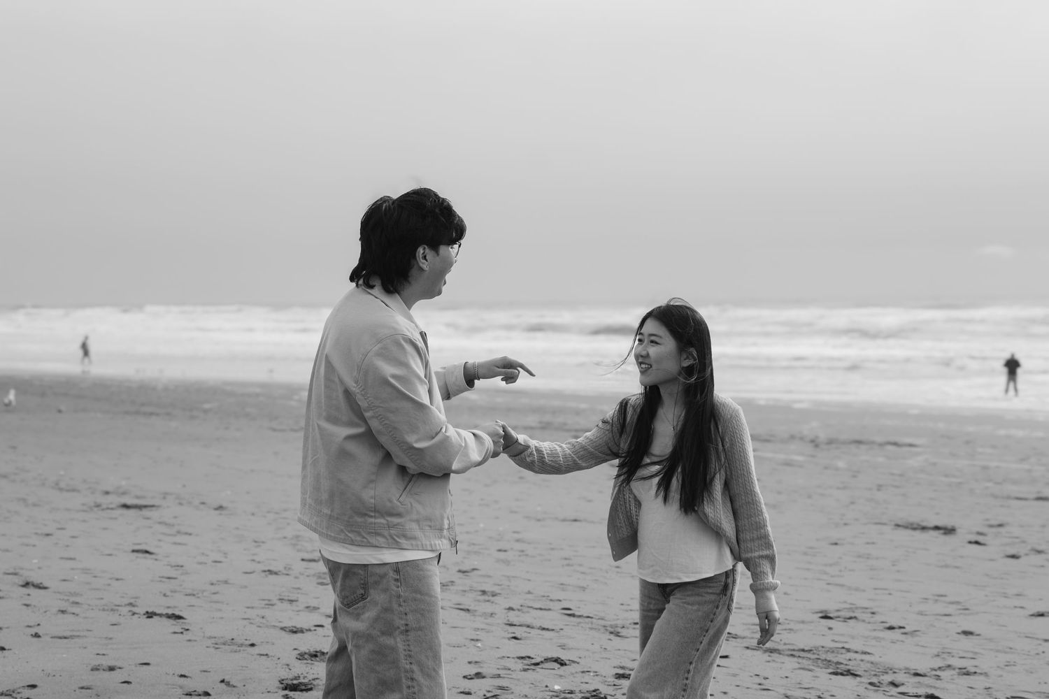 A couple having an animated conversation while walking along a foggy beach.