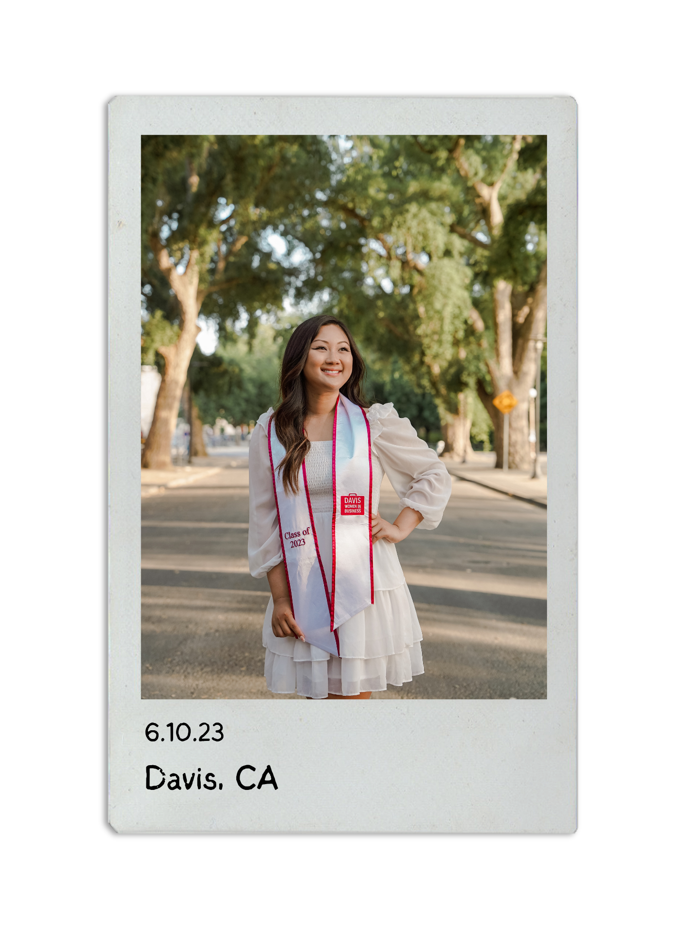 One of Allyson's grad photos in white dress and red stole standing on tree-lined path at UC Davis campus.