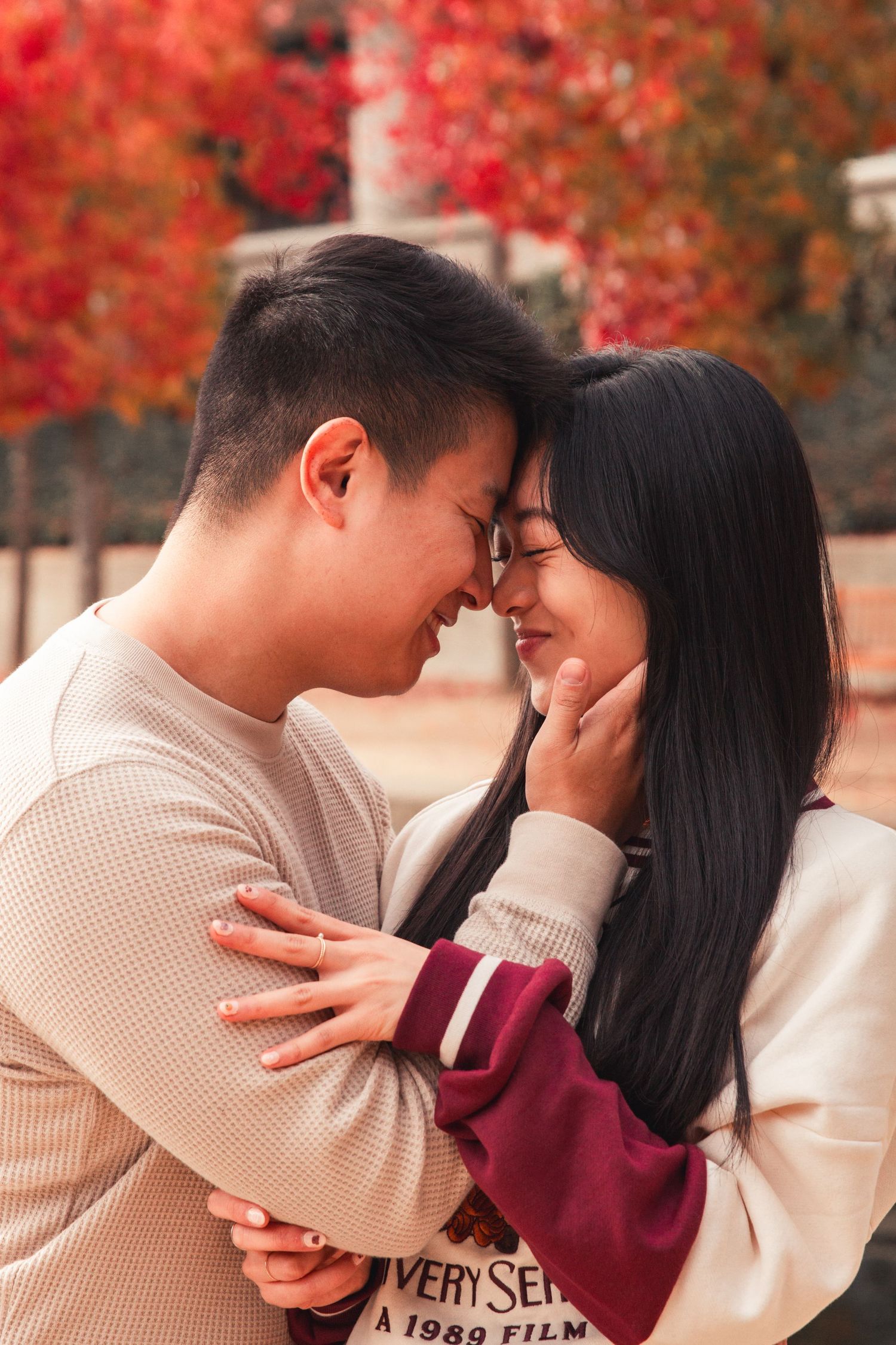 Intimate couple embracing with red fall foliage in background.