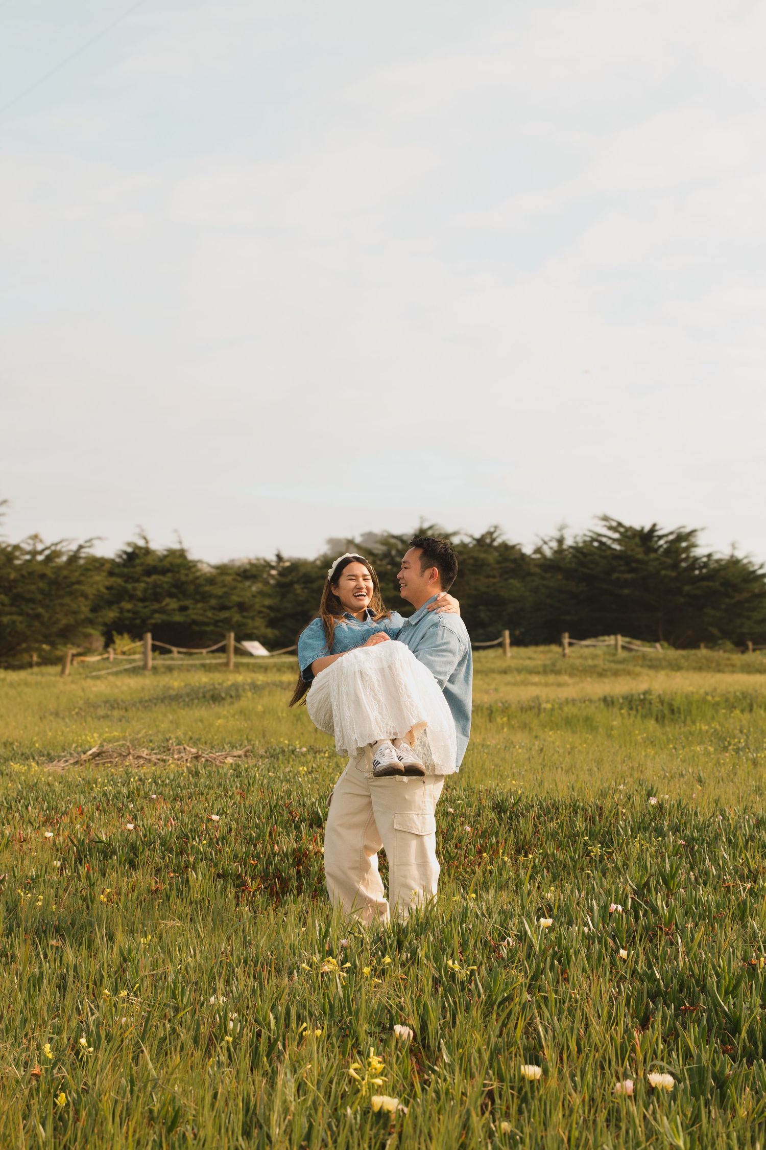 Couple embracing in a sunny meadow filled with wildflowers during golden hour.