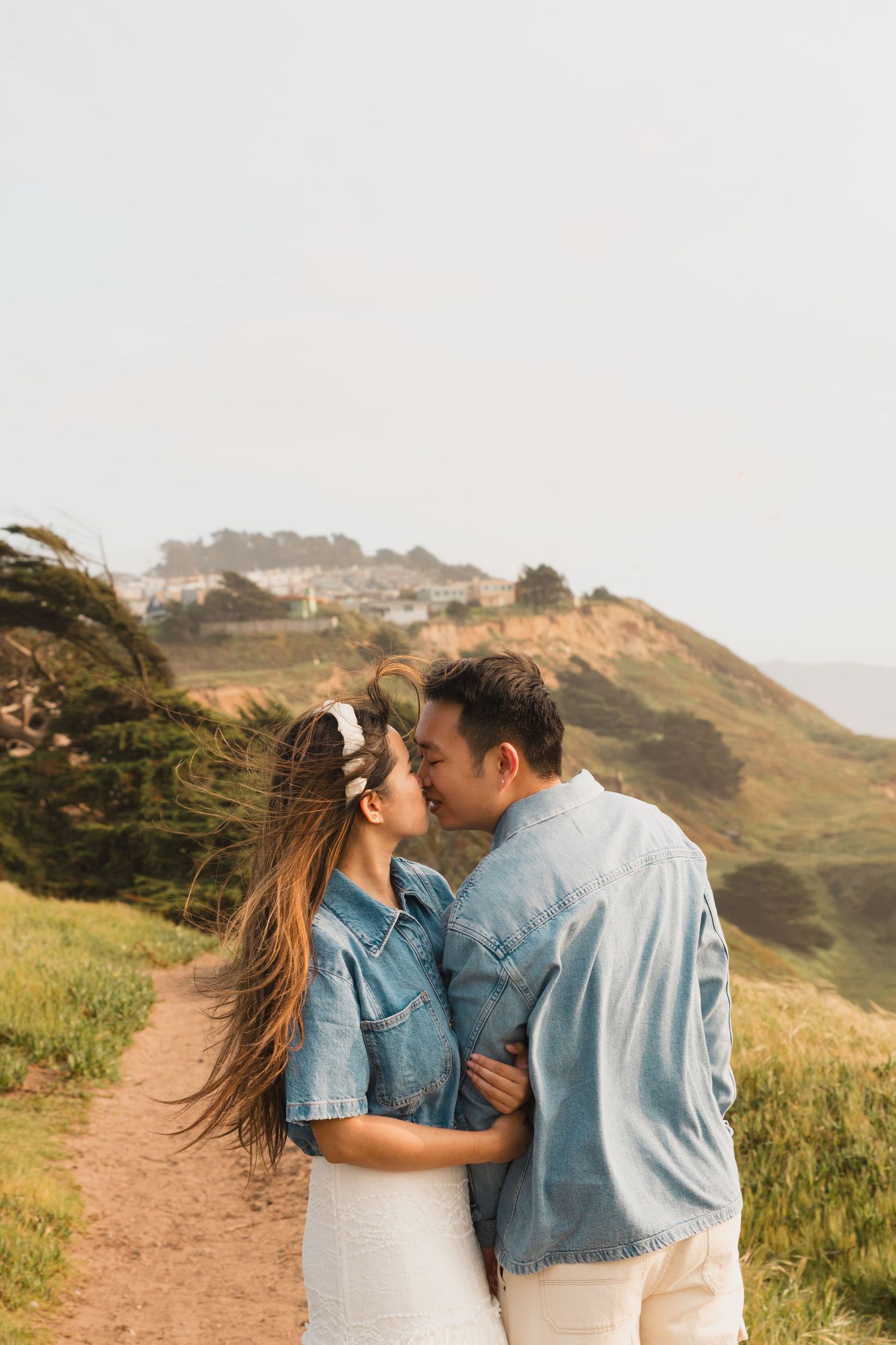 A couple in matching denim embraces on a scenic coastal path at sunset.