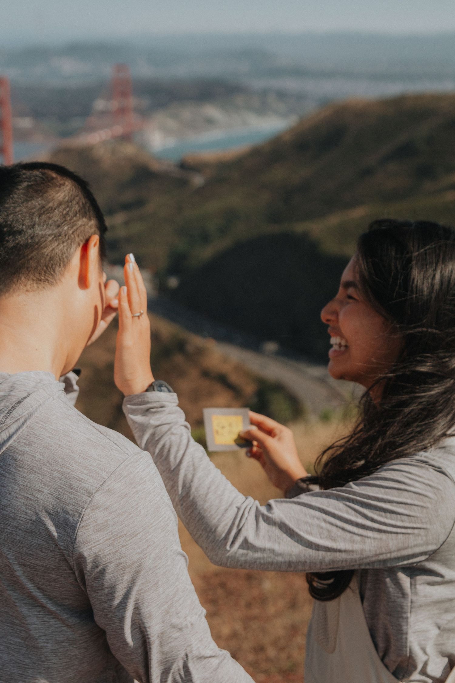 Couple playfully interacting with the Golden Gate Bridge and San Francisco cityscape in the background.
