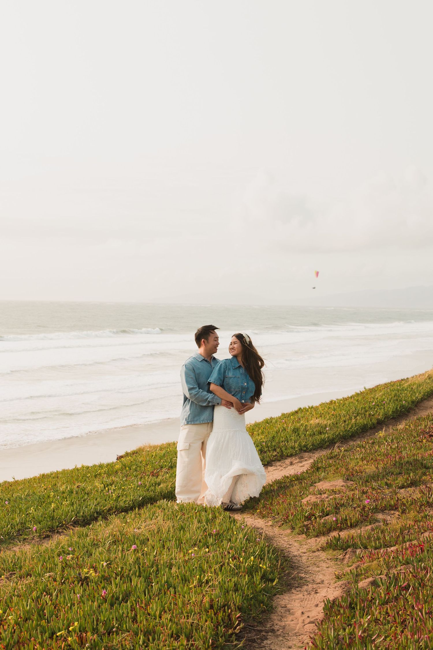A couple shares an intimate moment on a grassy coastal trail overlooking the ocean.