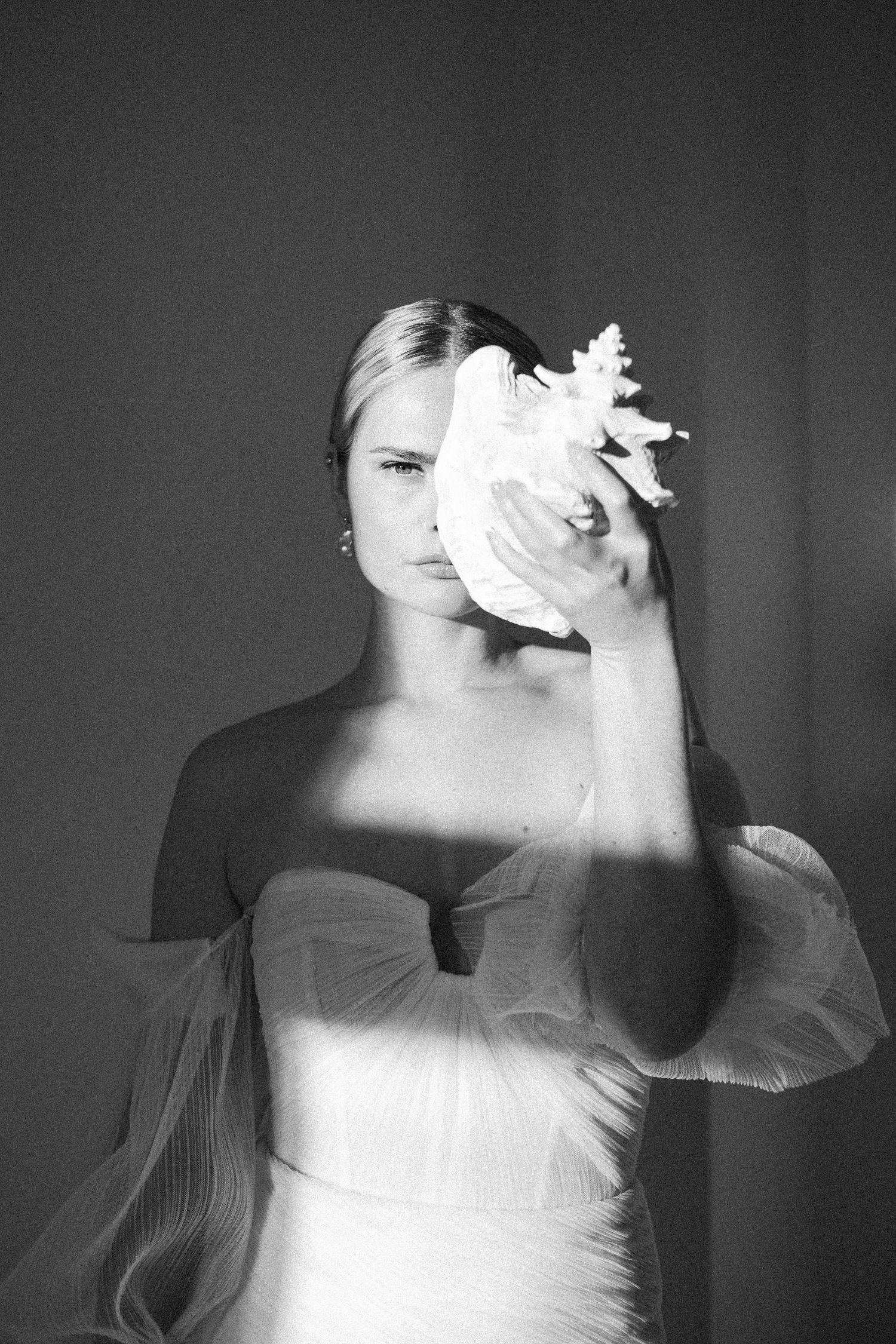 A black and white artistic portrait of a bride in white fabric holding a large flower in front of their face.