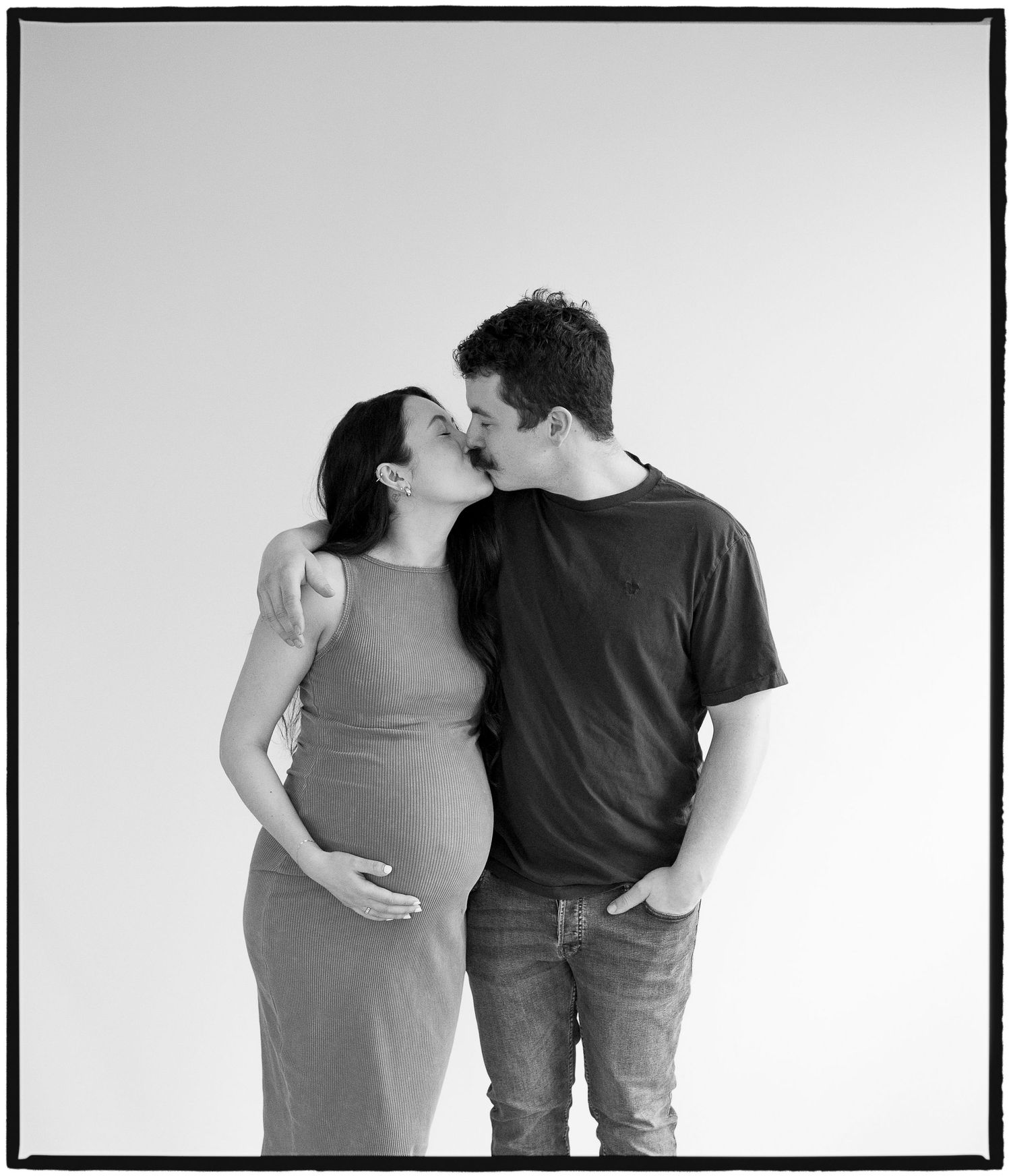 Intimate black and white portrait of an expecting couple against white background.