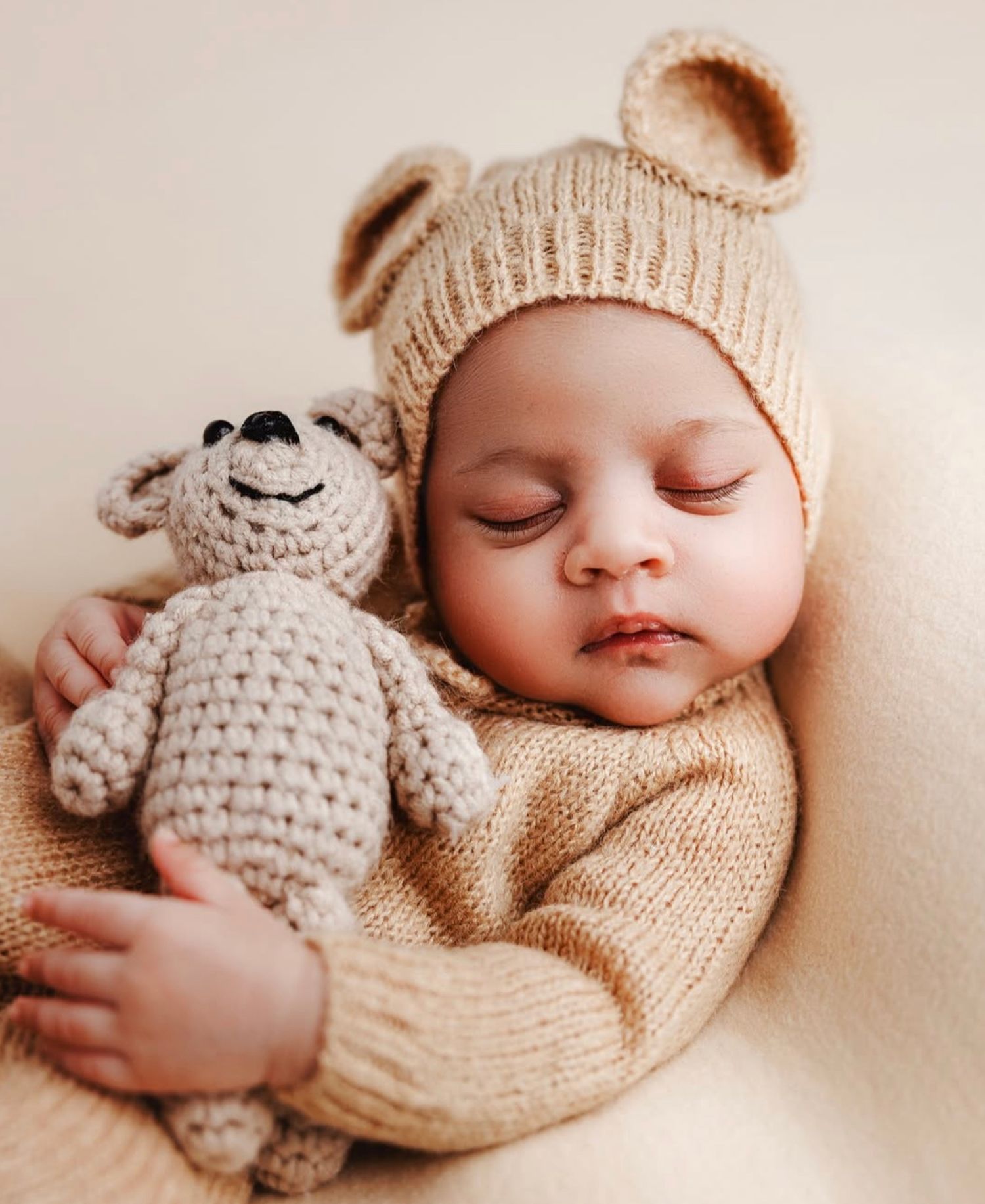 Newborn peacefully sleeps, holding a soft teddy bear while dressed in a cozy beige outfit, perfectly styled for their newborn session