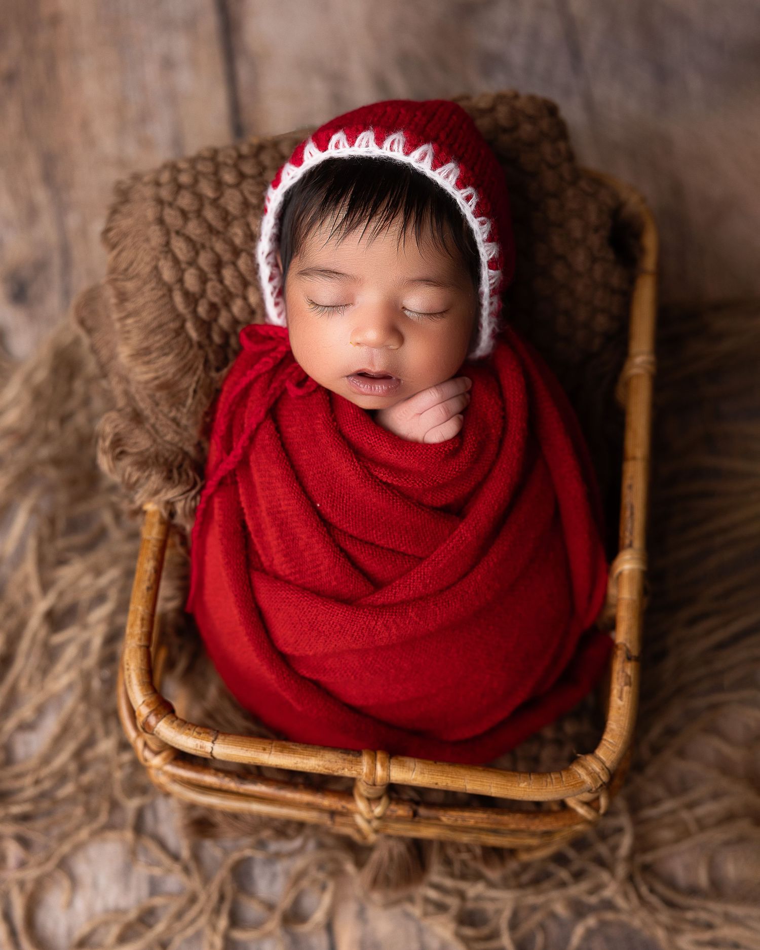 Cozy and calm newborn baby wrapped in red, resting in a rectangular basket during a Seattle studio portrait session.