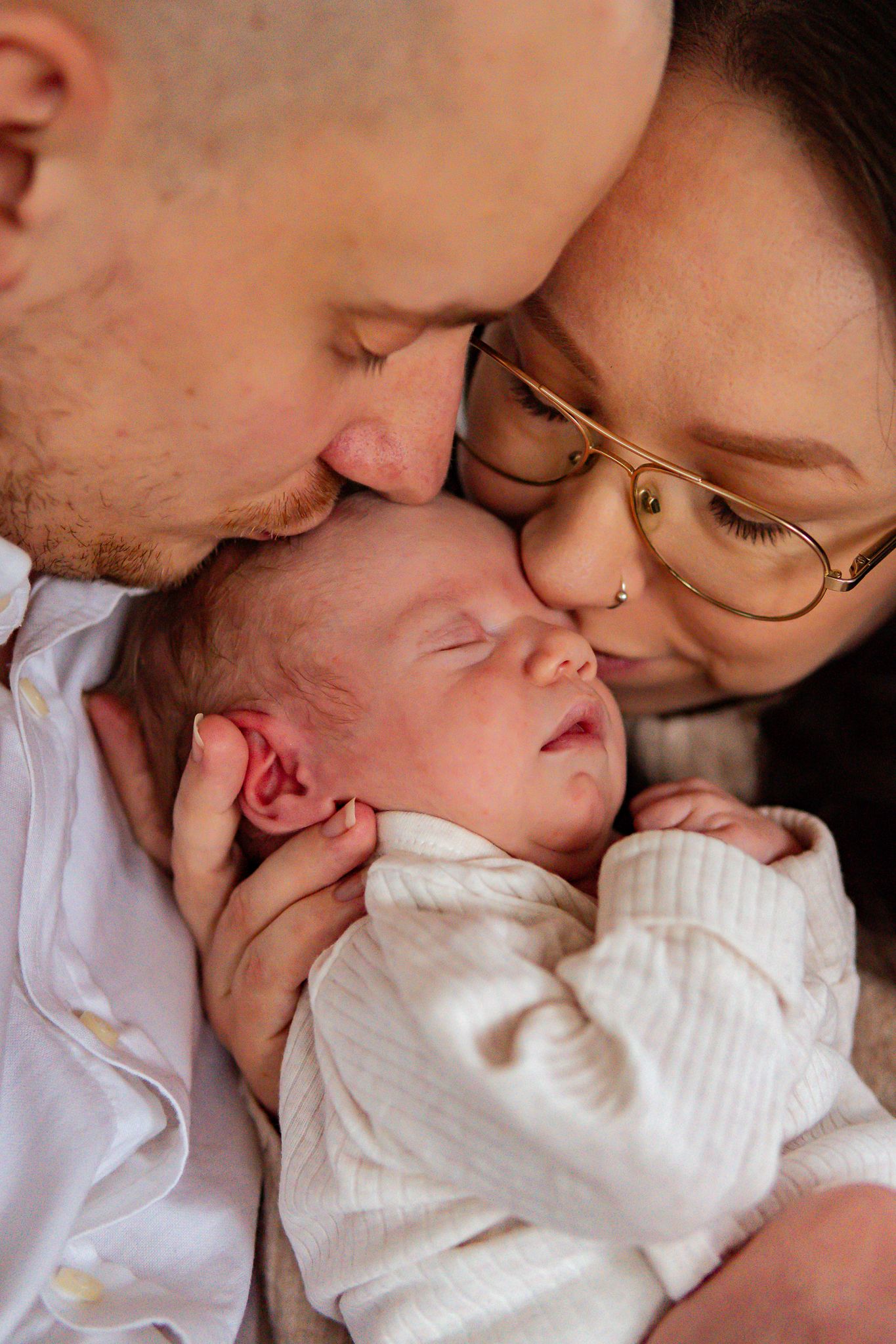 Kärleksfullt ögonblick mellan föräldrar och deras nyfödda sovande bebis, där alla är nära och bebis får pussar på huvudet. Nyföddfotograf