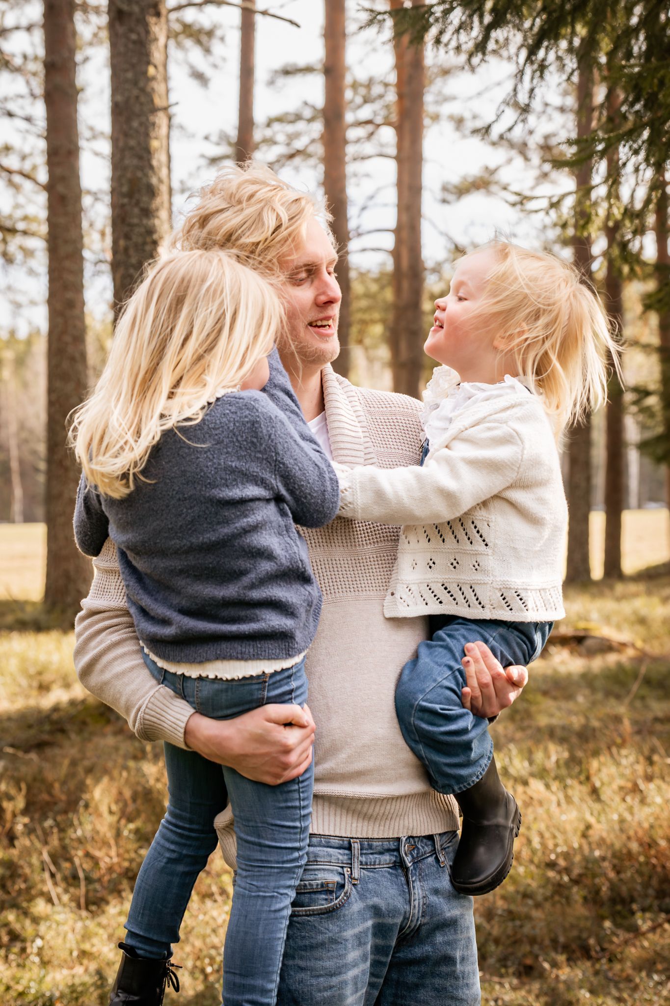 En pappa har sina döttrar i famnen som skrattar med skogen som bakgrund. Fotograf, familjefotograf, Umeå, Västerbotten