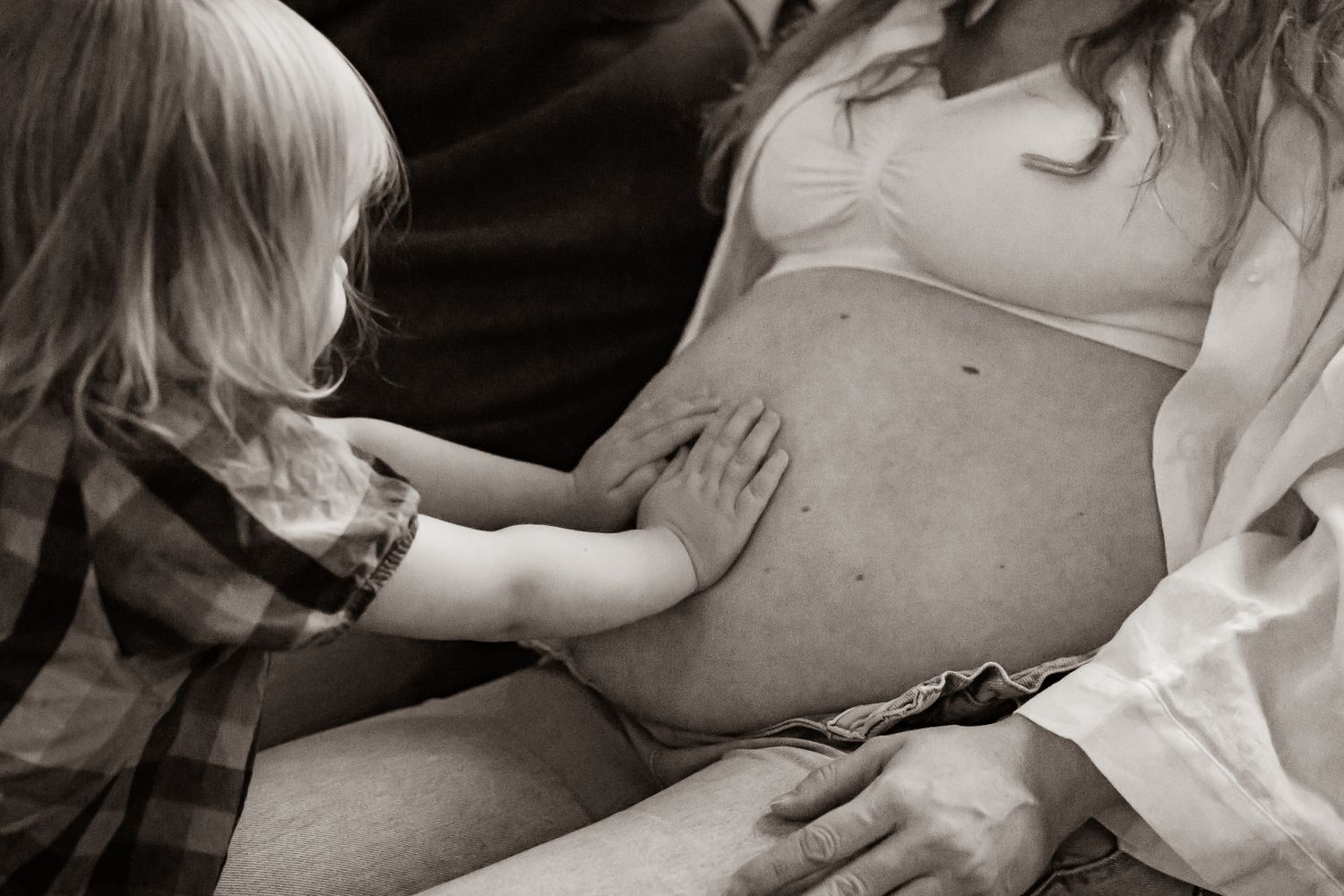 Svartvit bild på en liten tjej som håller händerna kärleksfullt på mammas gravida mage. Gravidfotograf, Umeå, Västerbotten