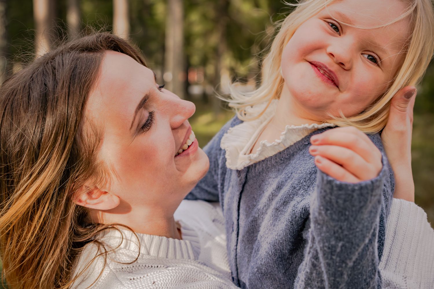 En mamma tittar kärleksfullt på sin busiga dotter i famnen med skogen som bakgrund och varmt solljus. Fotograf, familjefotograf, Umeå