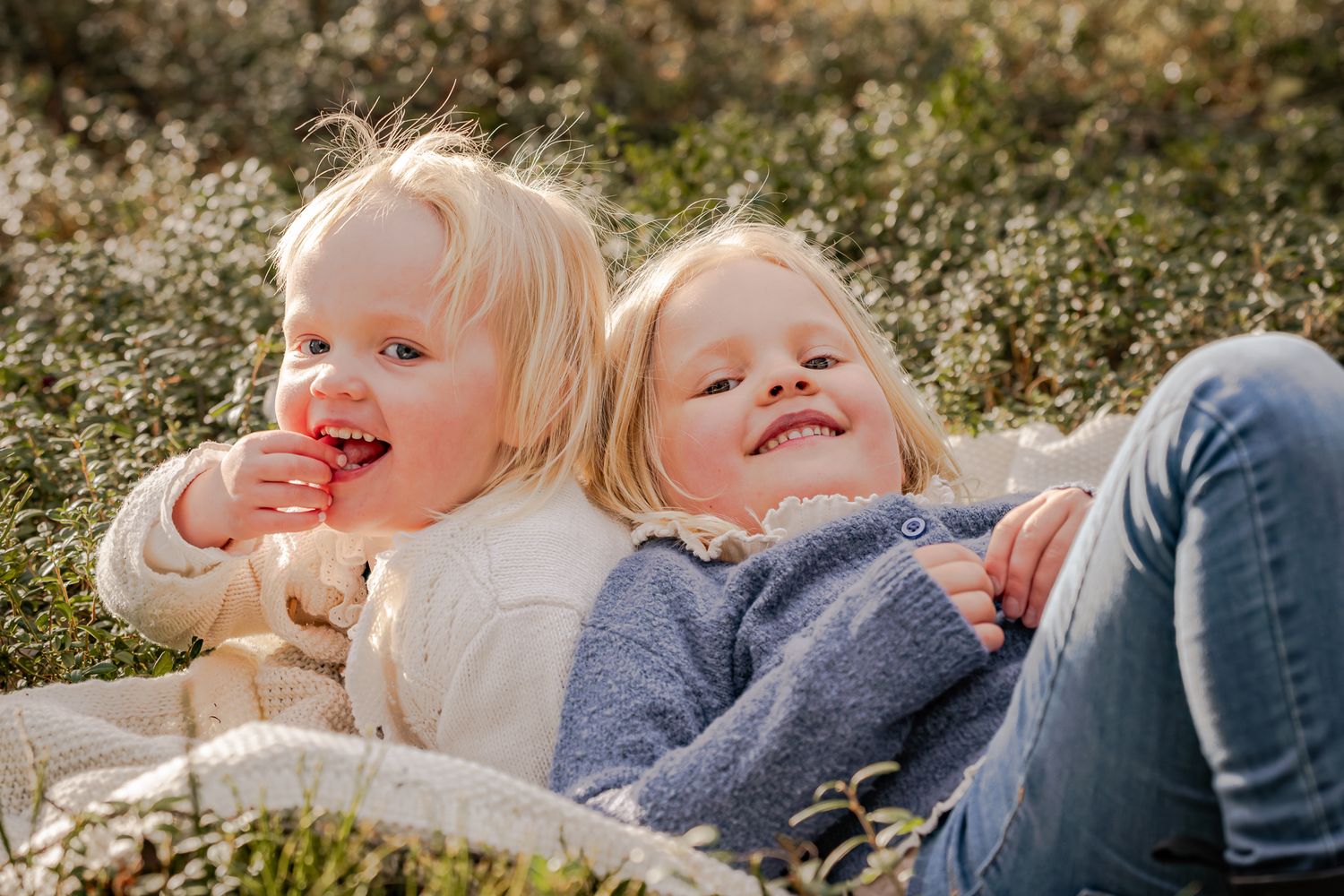 Två systrar som ligger tillsammans på en filt i skogen och ler. Fotograf, familjefotograf, Umeå, Västerbotten