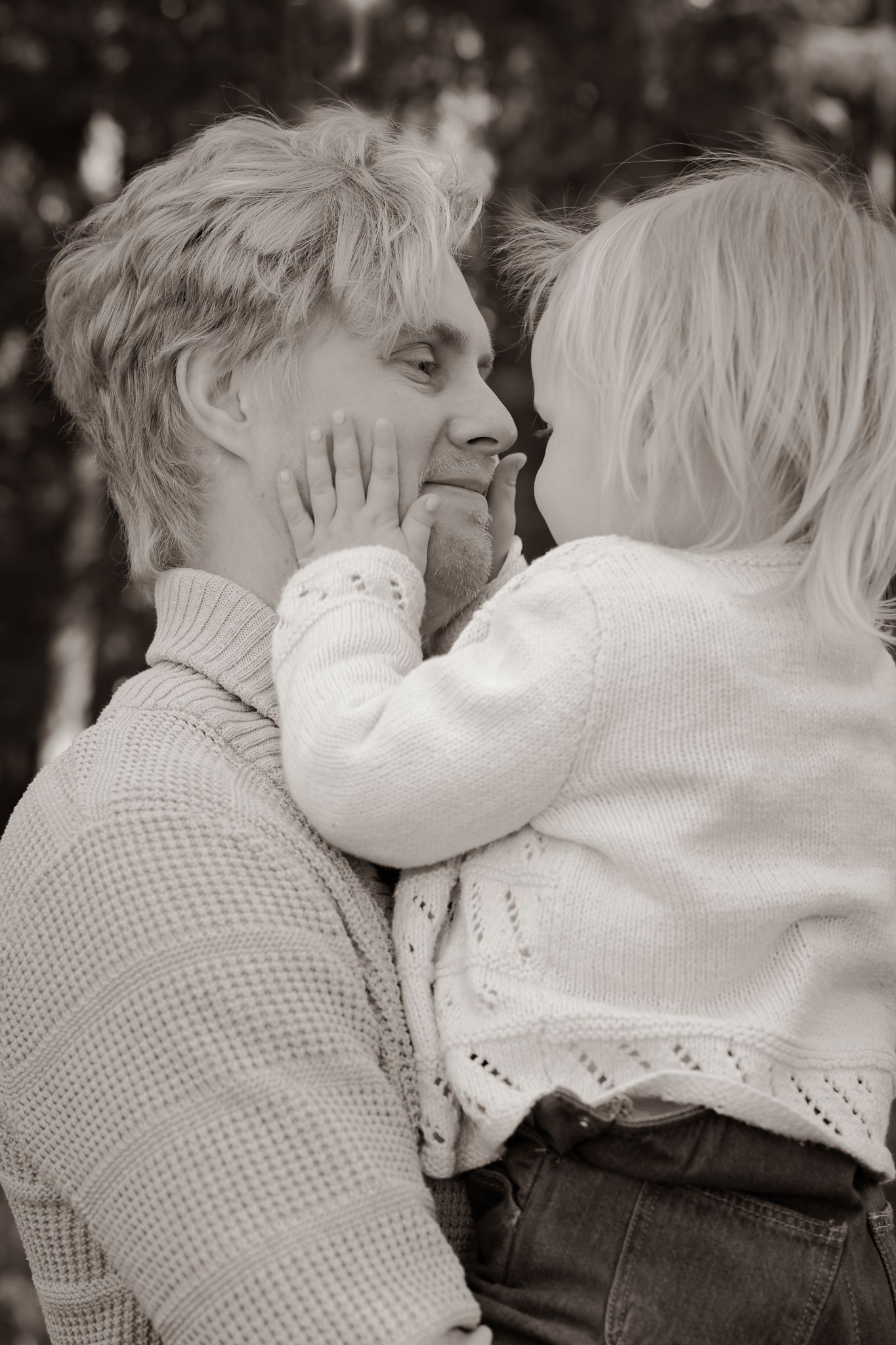 Svartvit bild på pappa med dotter i famnen som håller händerna på hans kinder. Fotograf, familjefotograf, Umeå, Västerbotten