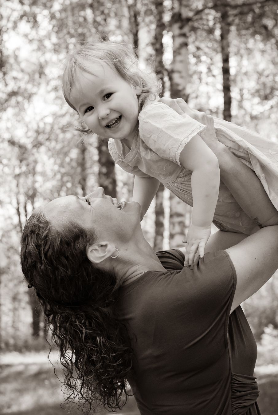 Svartvit bild av ett ömt ögonblick där en mamma lyfter upp sin dotter i luften i en skogsmiljö. Fotograf, Familjefotograf, Umeå
