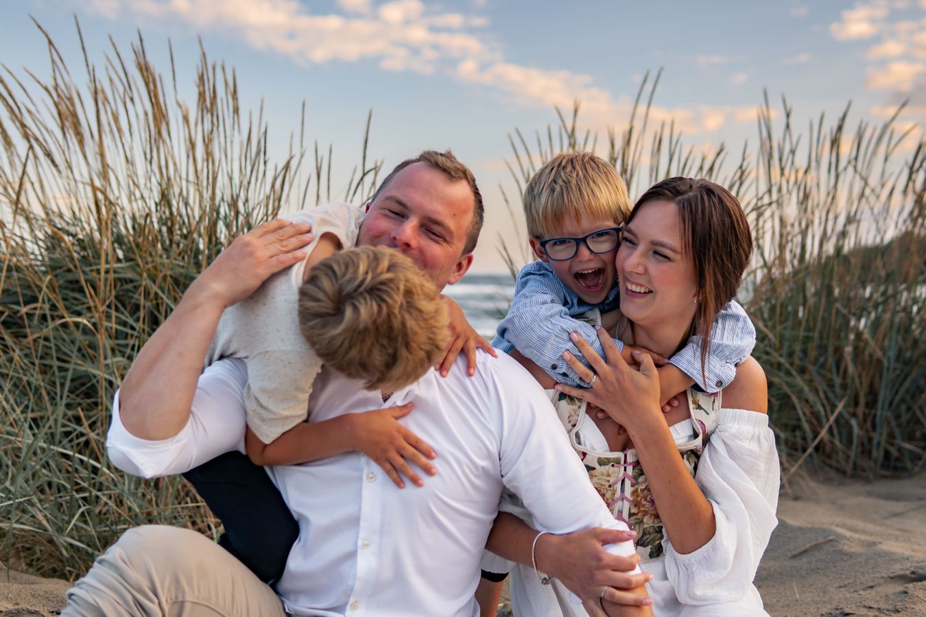 En familj delar ett glädjefyllt och kärleksfullt ögonblick tätt intill varandra på stranden i solnedgången. Familjefotograf, Umeå