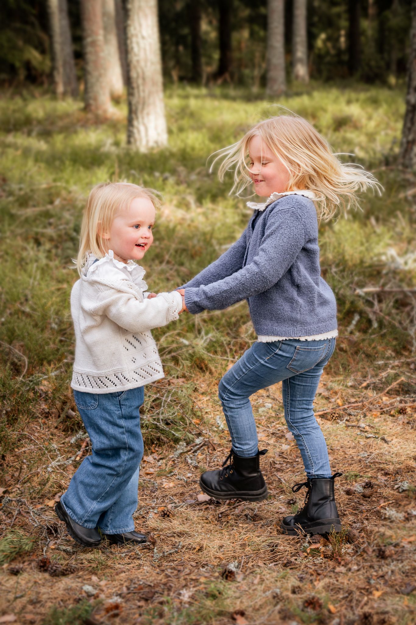 Två glada systrar som dansar runt hand i hand i skogen. Fotograf, familjefotograf, Umeå, Västerbotten