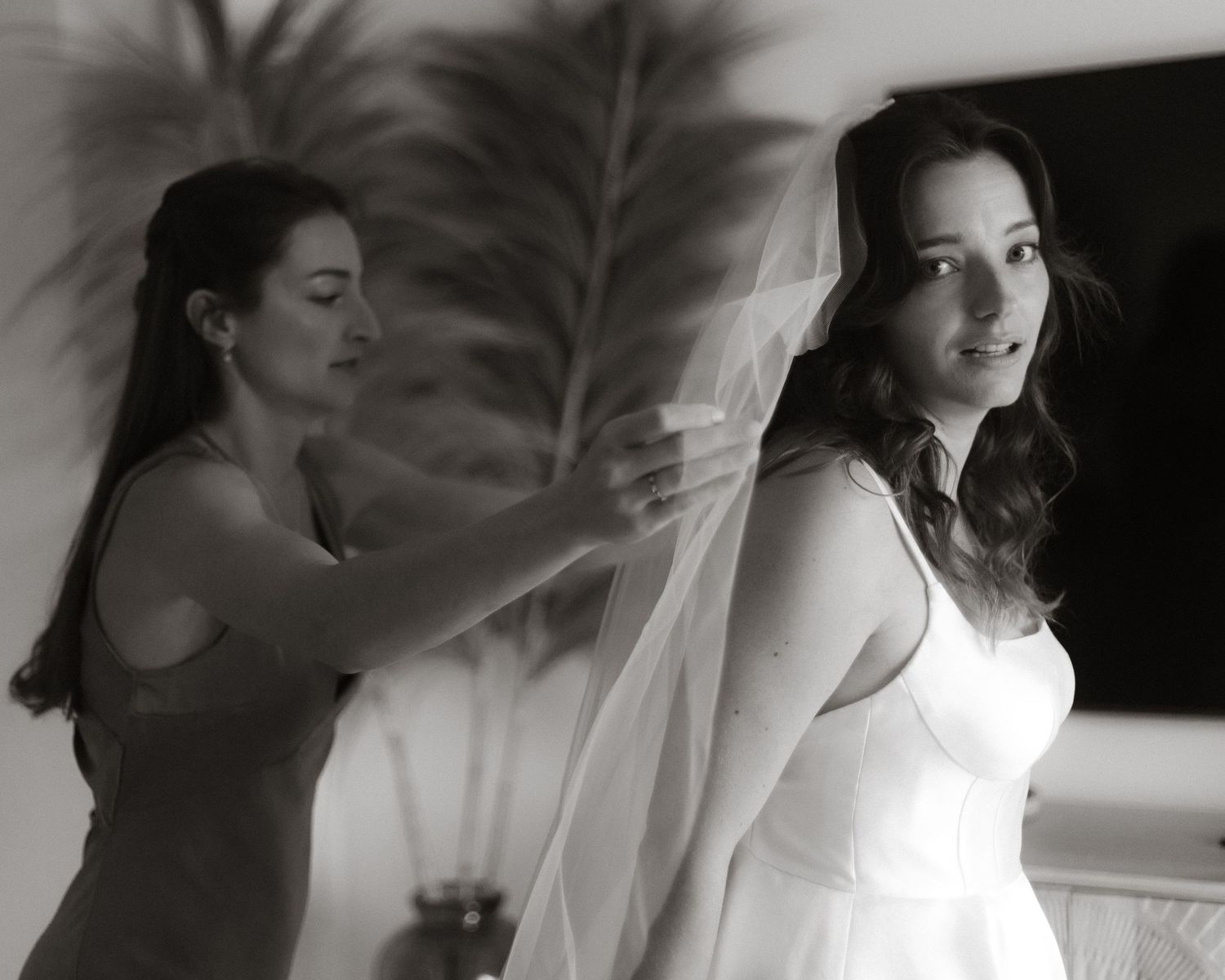 Black and white photo showing preparation during a bridal fitting with a veil and formal wedding gown.