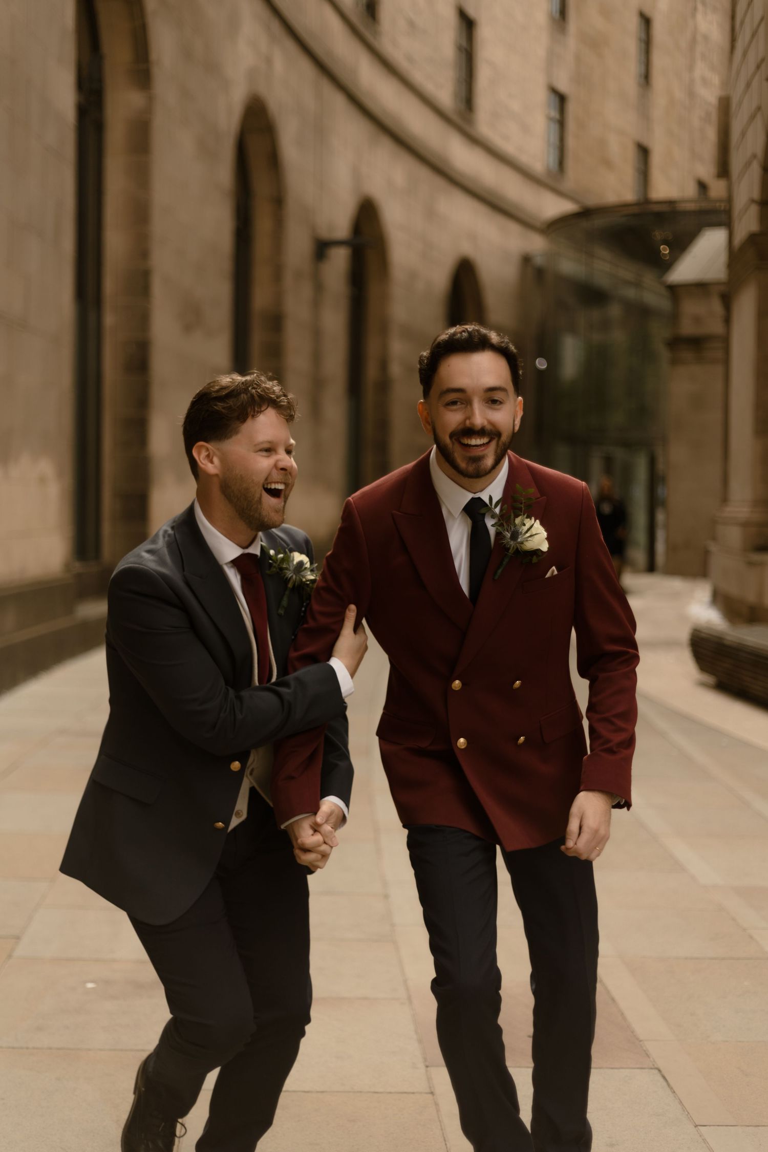 Two people in formal suits walking and laughing together along an urban stone walkway in warm sepia tones.