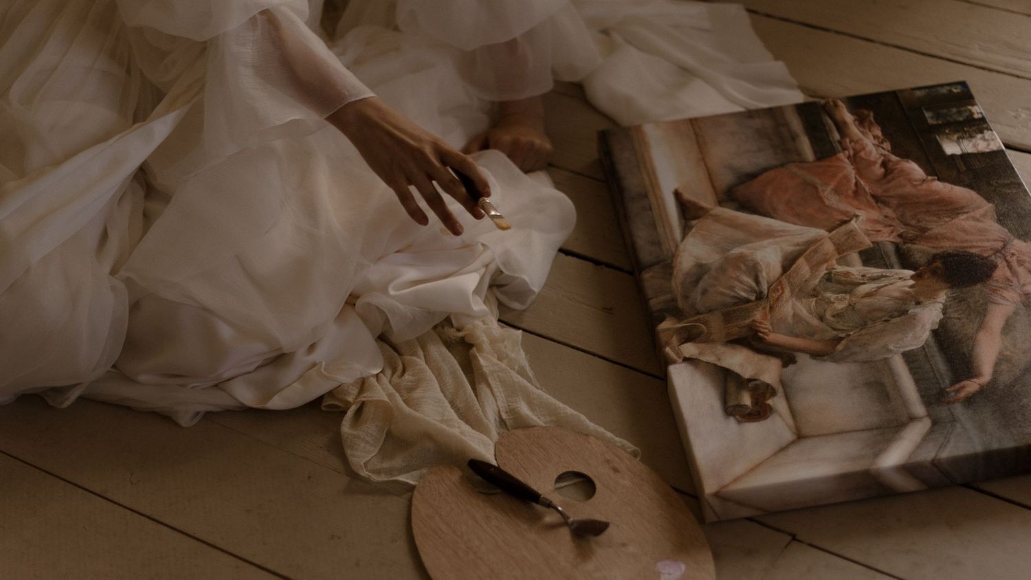 A white wedding dress and hands delicately arranged on a wooden floor with old photographs nearby.