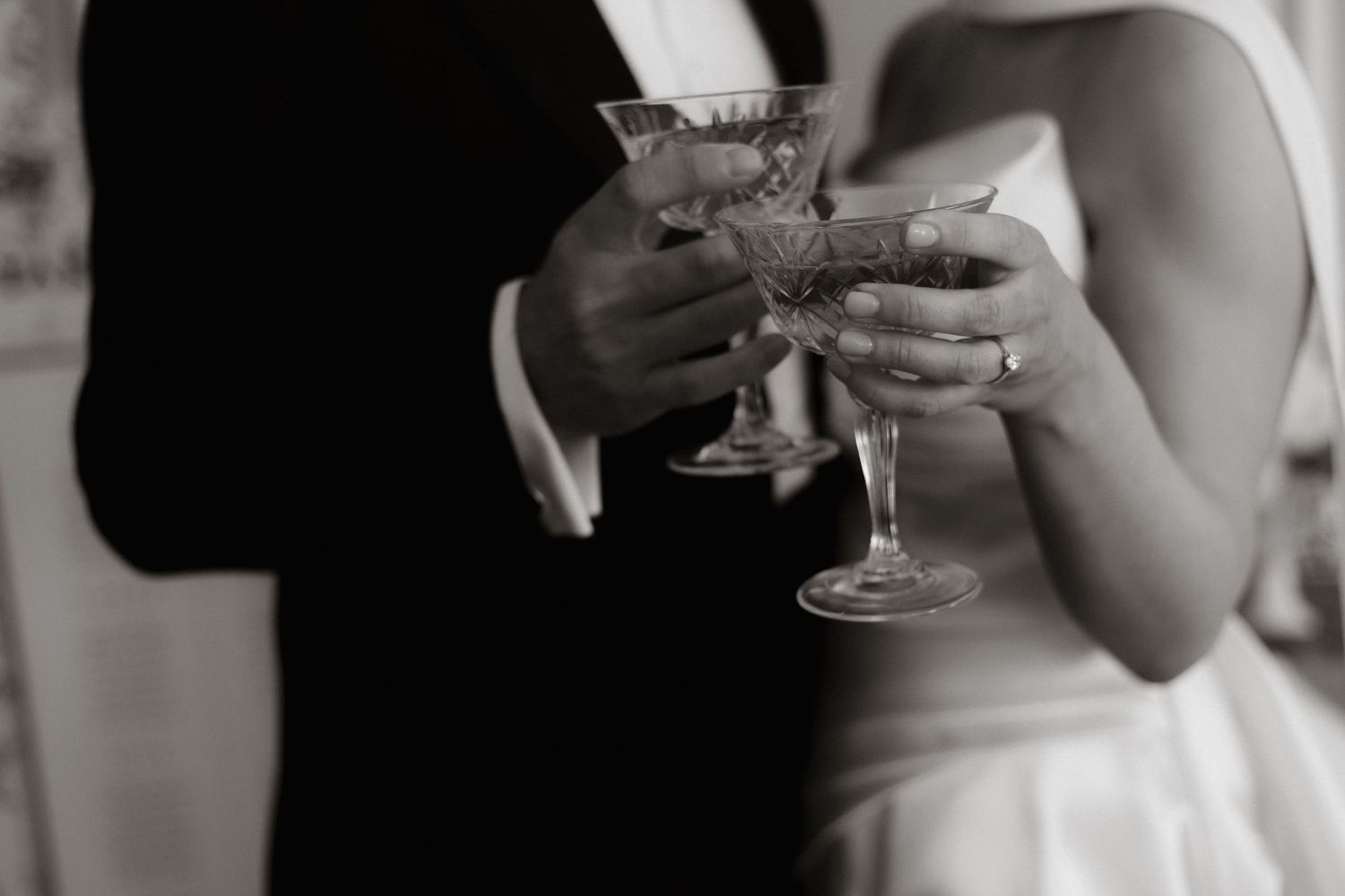 Black and white closeup of hands holding a crystal martini glass at a formal event.
