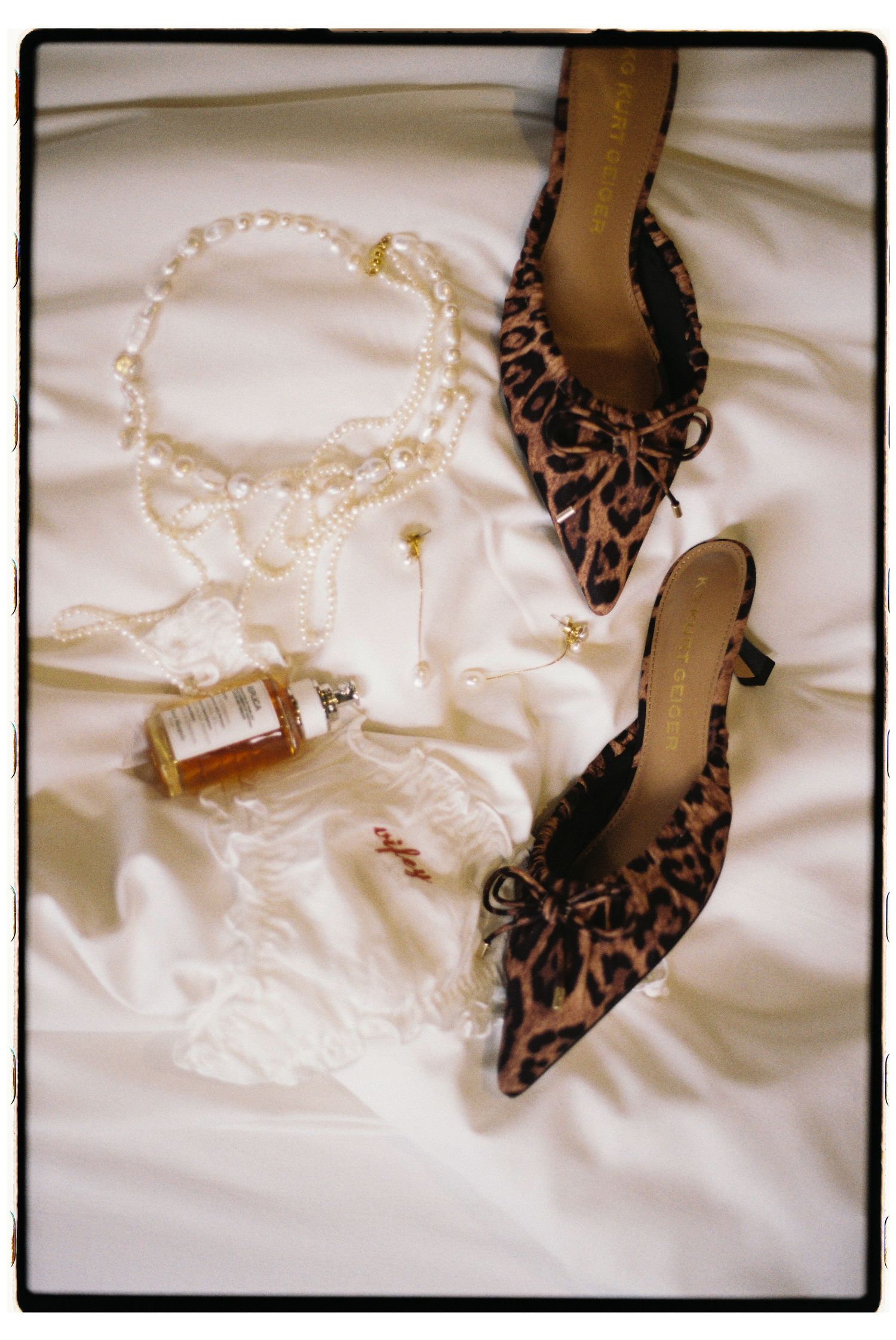 Leopard print high heel shoes are displayed against white satin fabric alongside a delicate pearl necklace.
