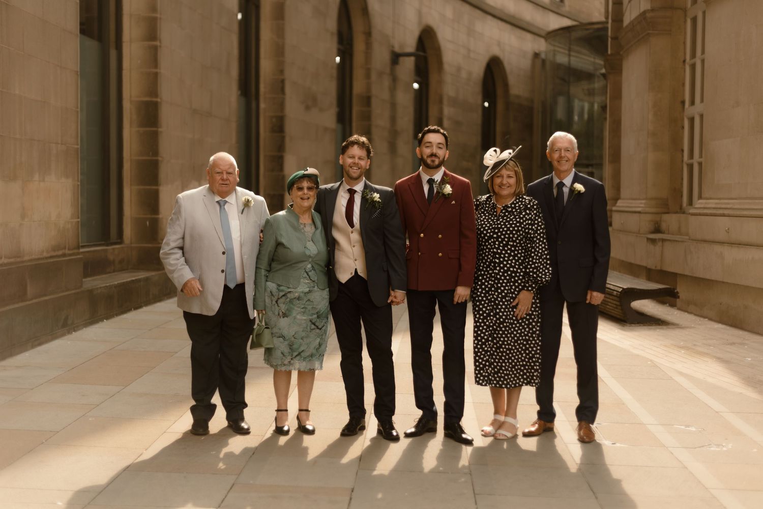 Group standing together in an elegant hallway with columns, dressed in formal vintage-inspired attire.