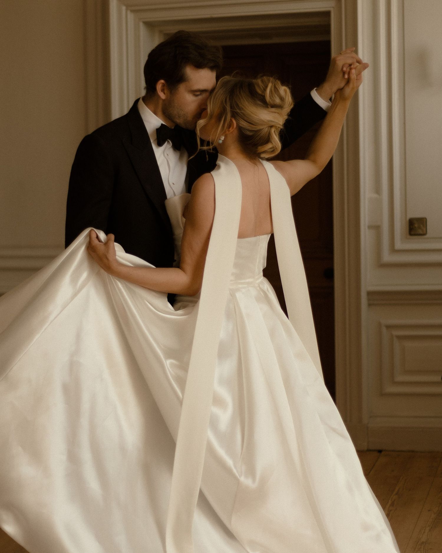 A tender moment between newlyweds as they embrace in a classic indoor setting, her elegant white gown flowing gracefully.